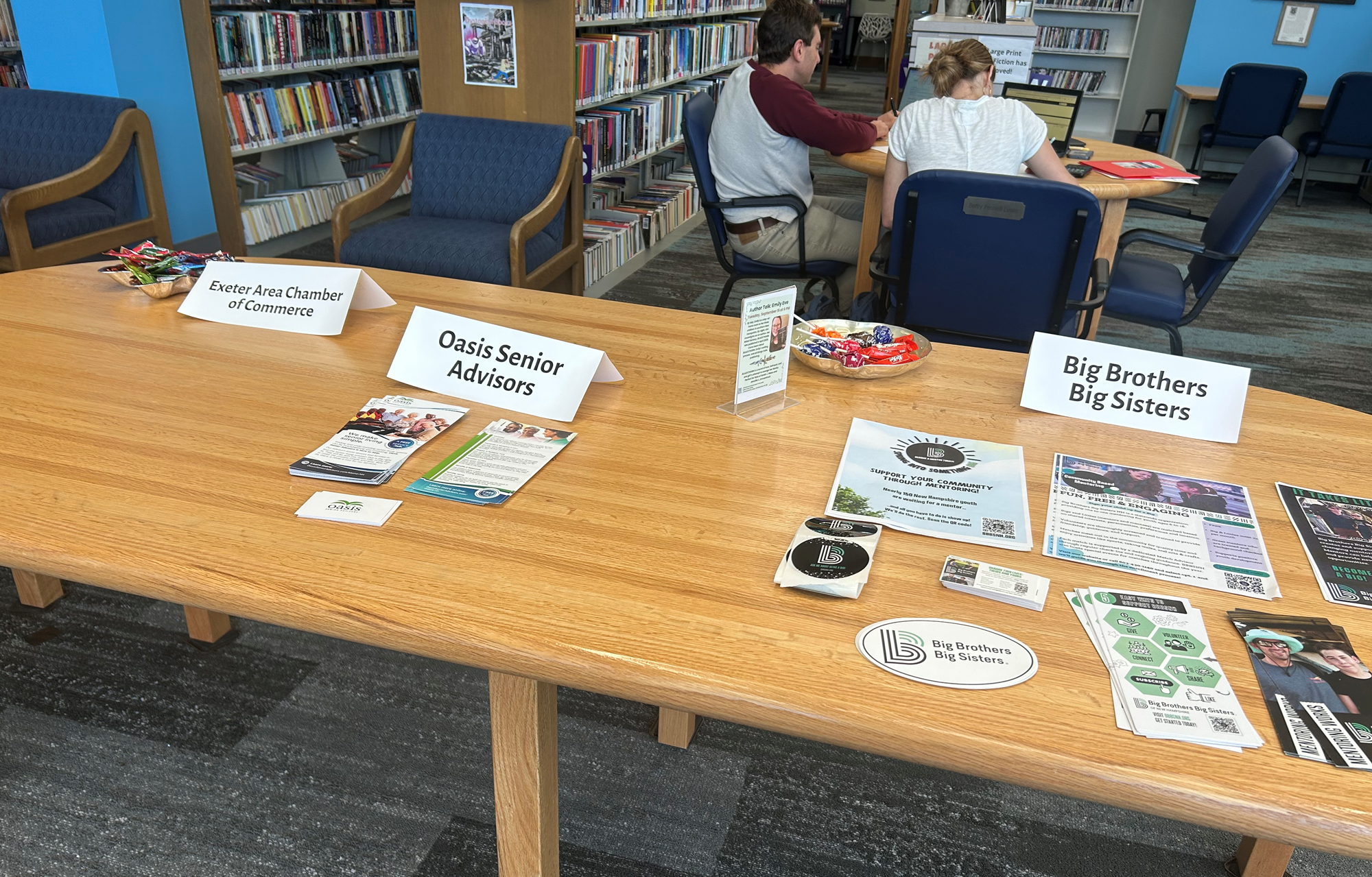 A table for Exeter Area Chamber of Commerce, Oasis Senior Advisors, and Big Brothers Big Sisters on the main floor of the library.