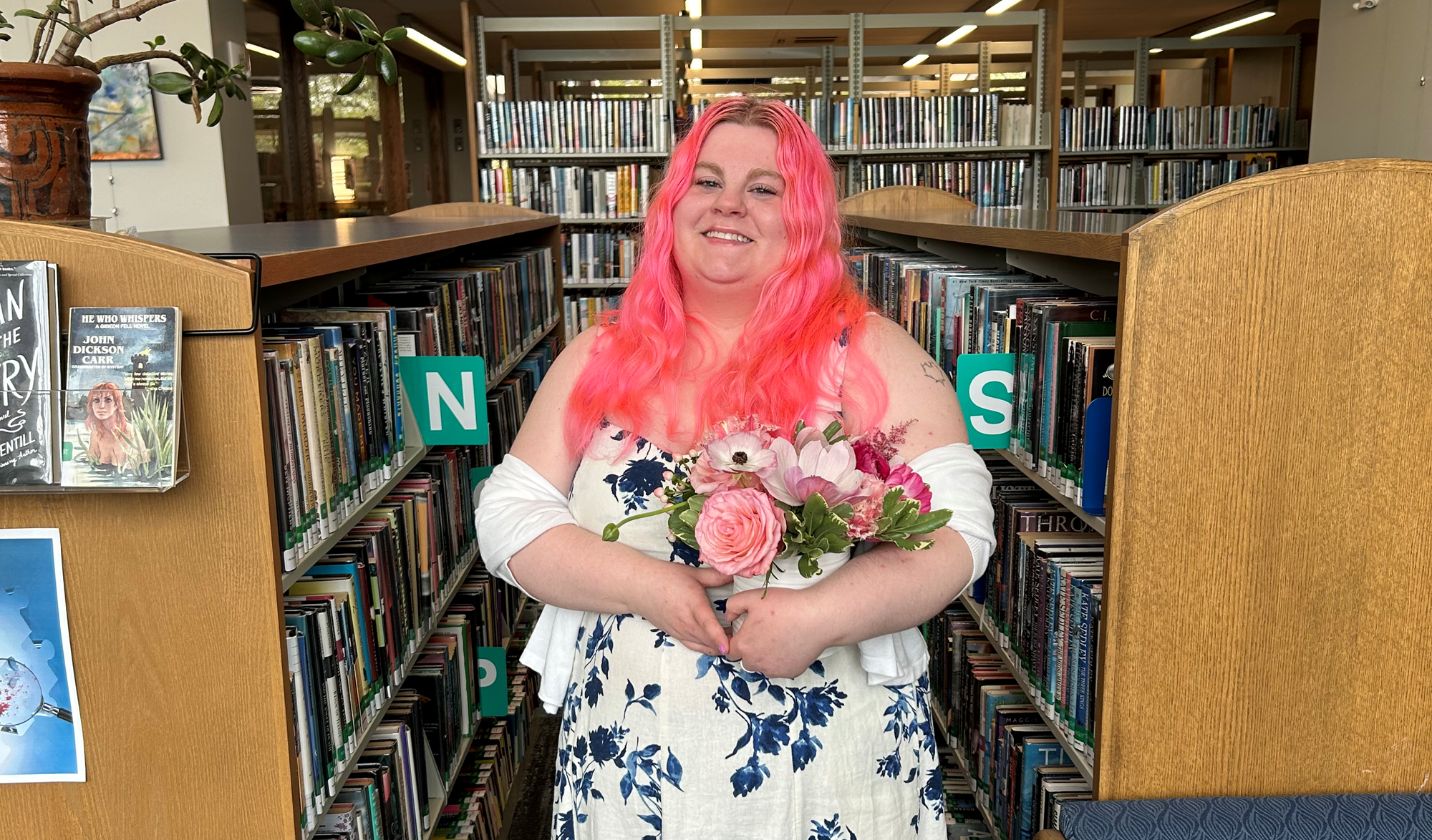 Staff member Loren posing with flowers in the Mystery Wing of the library. Staff member Loren posing with flowers in the Mystery Wing of the library.