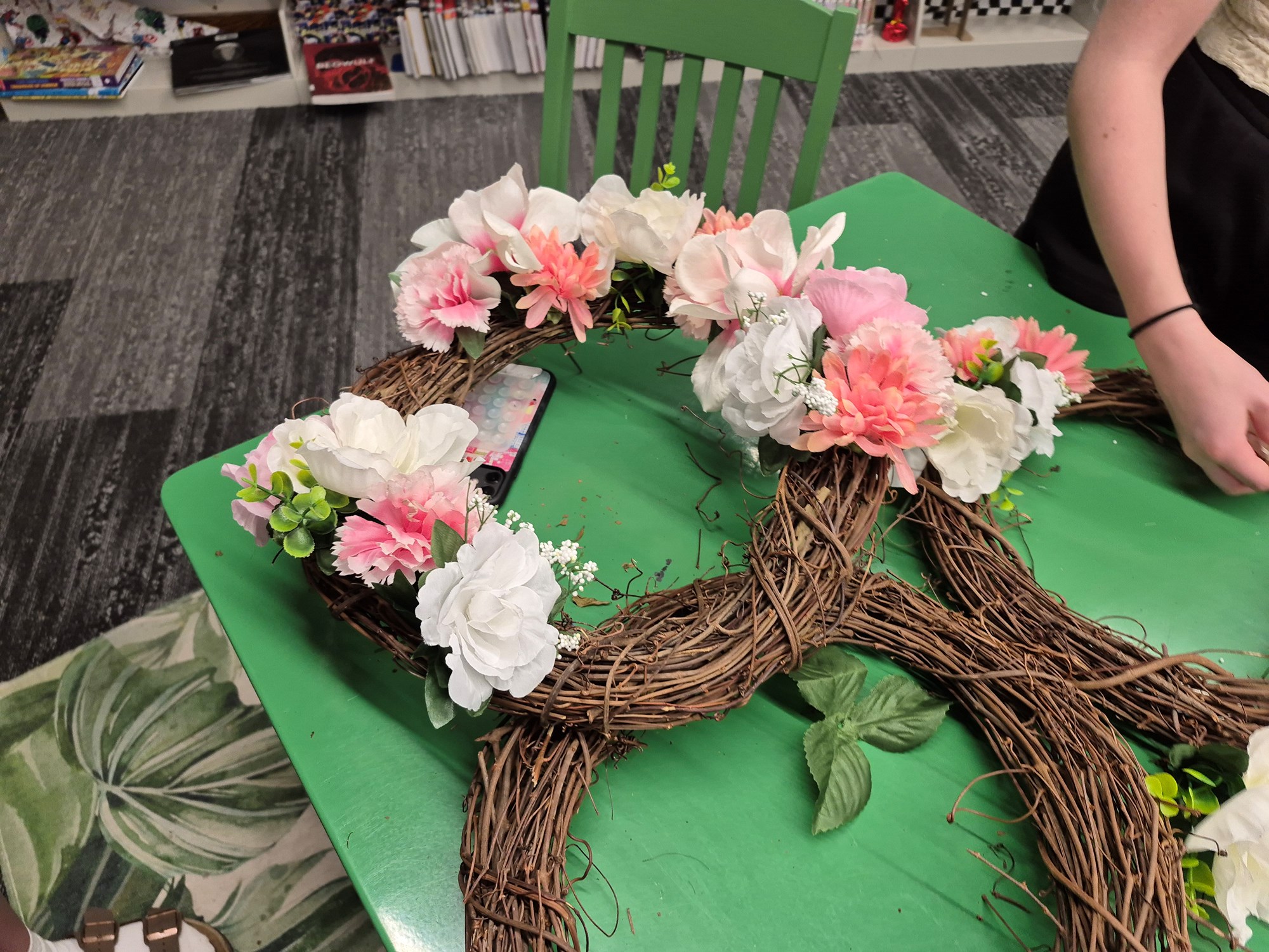 A flower wreath with white, pale pink, and deeper pink flowers on a green table in the Teen Scene.