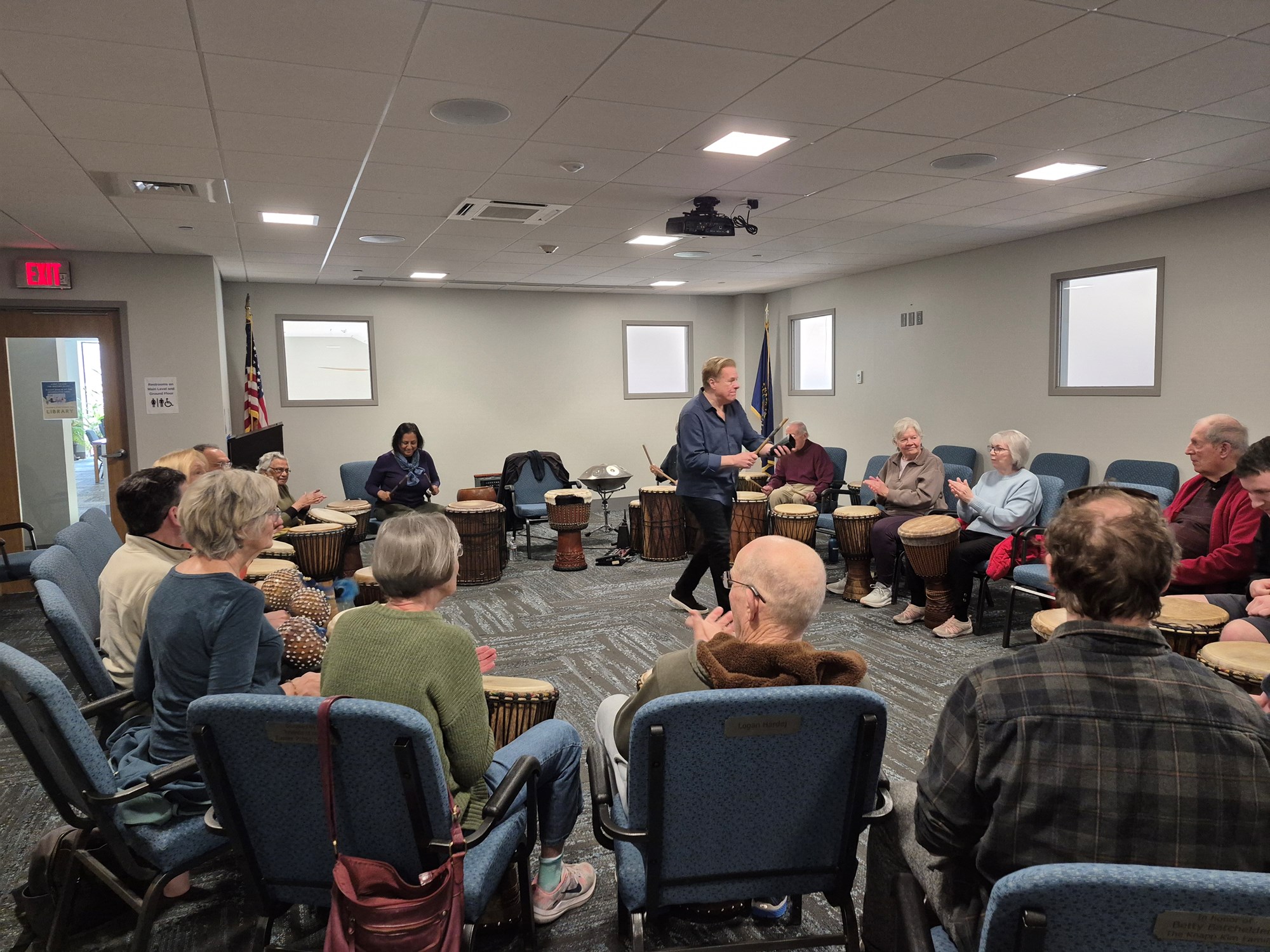 Randy Armstrong surrounded by a circle of patrons playing drums in the Meeting Room.