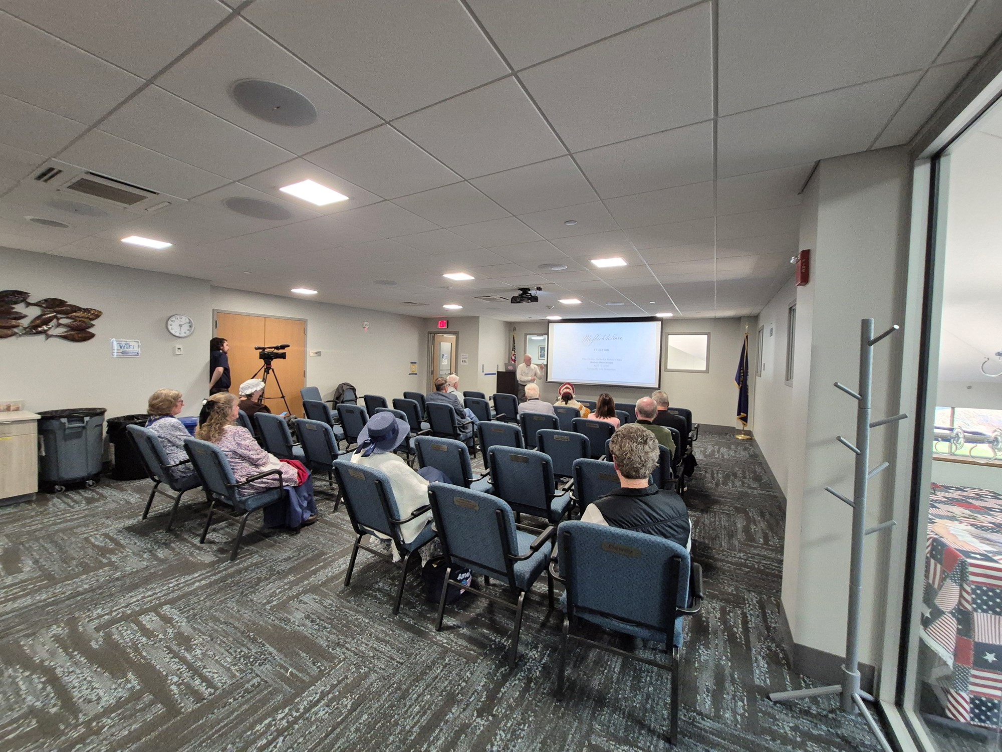 Far away shot of the presentation and spectators in the Meeting Room.
