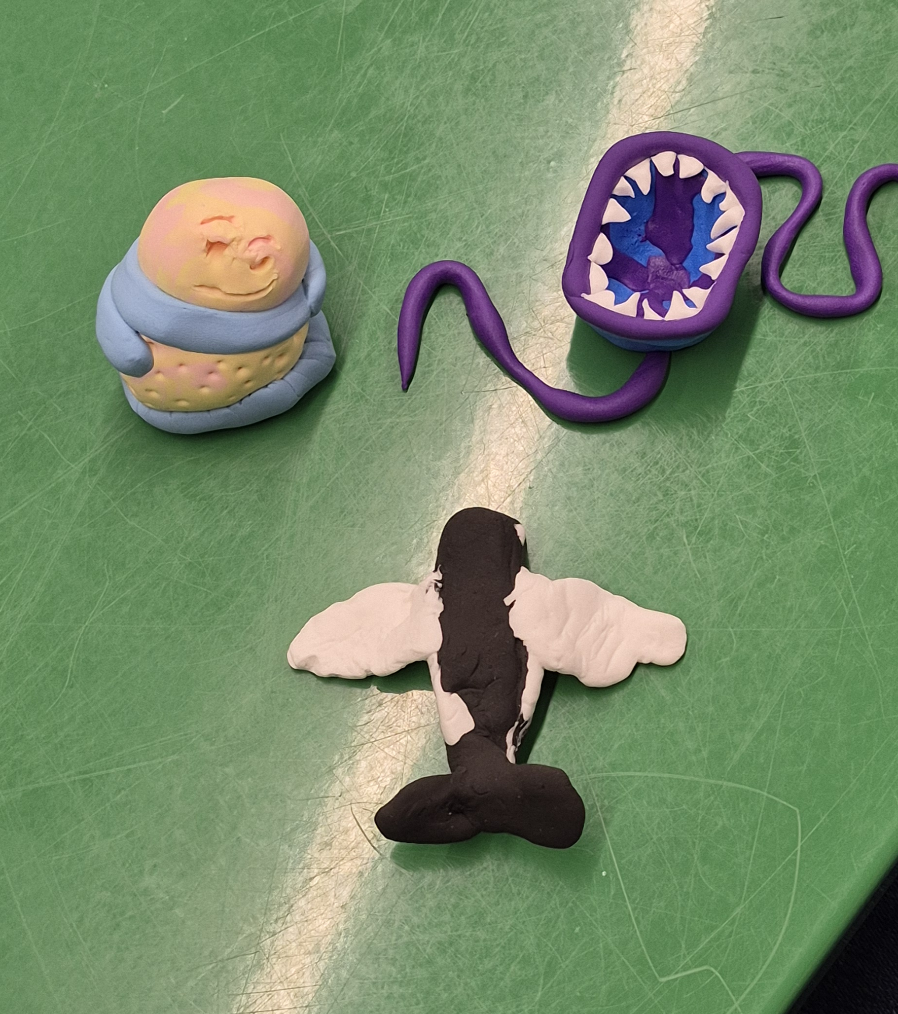 Three clay creatures, including a flying killer orca, on a green table in the Teen Scene. 