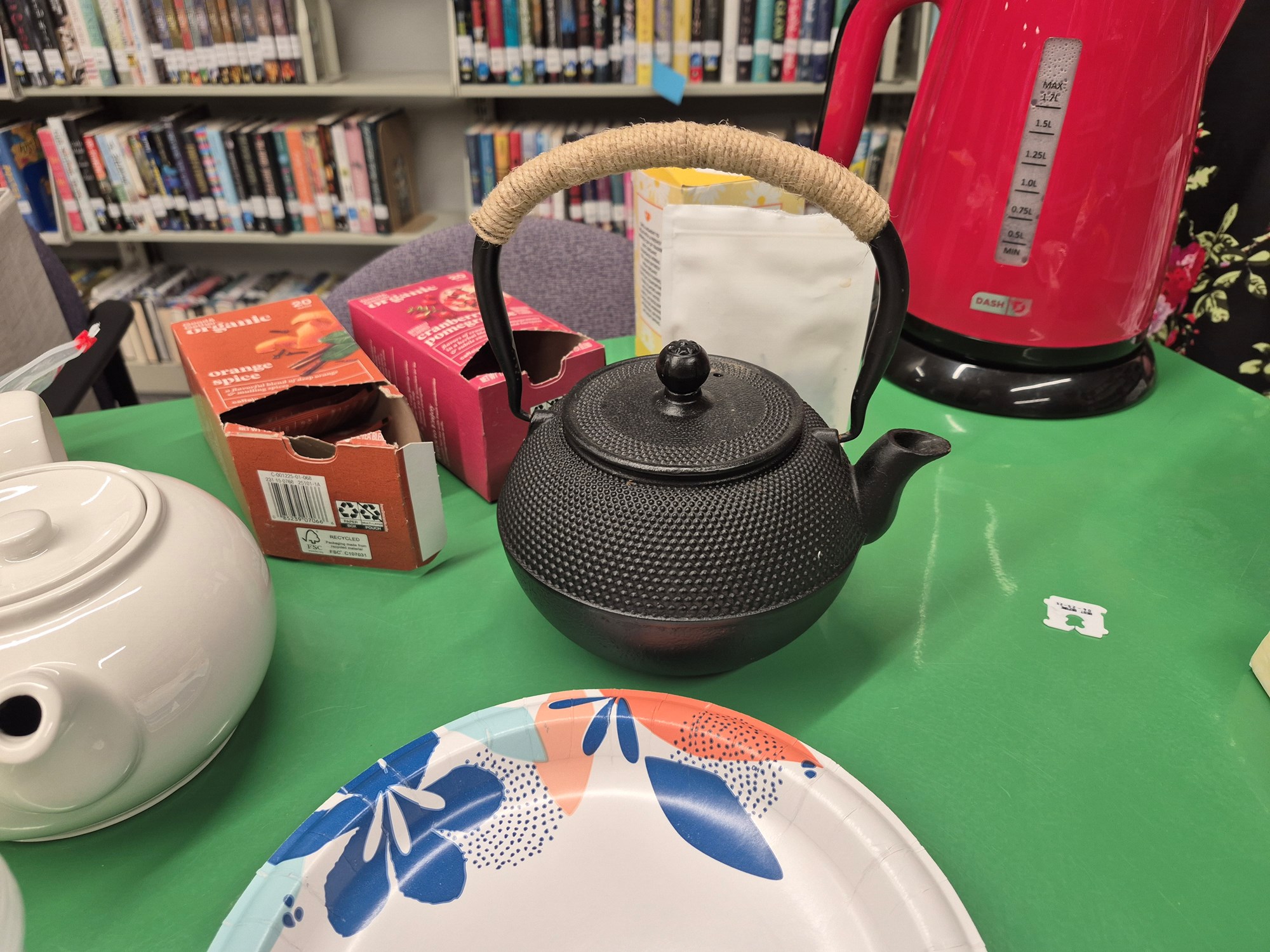 A black teapot and a white teapot on a green table in the Teen Scene.