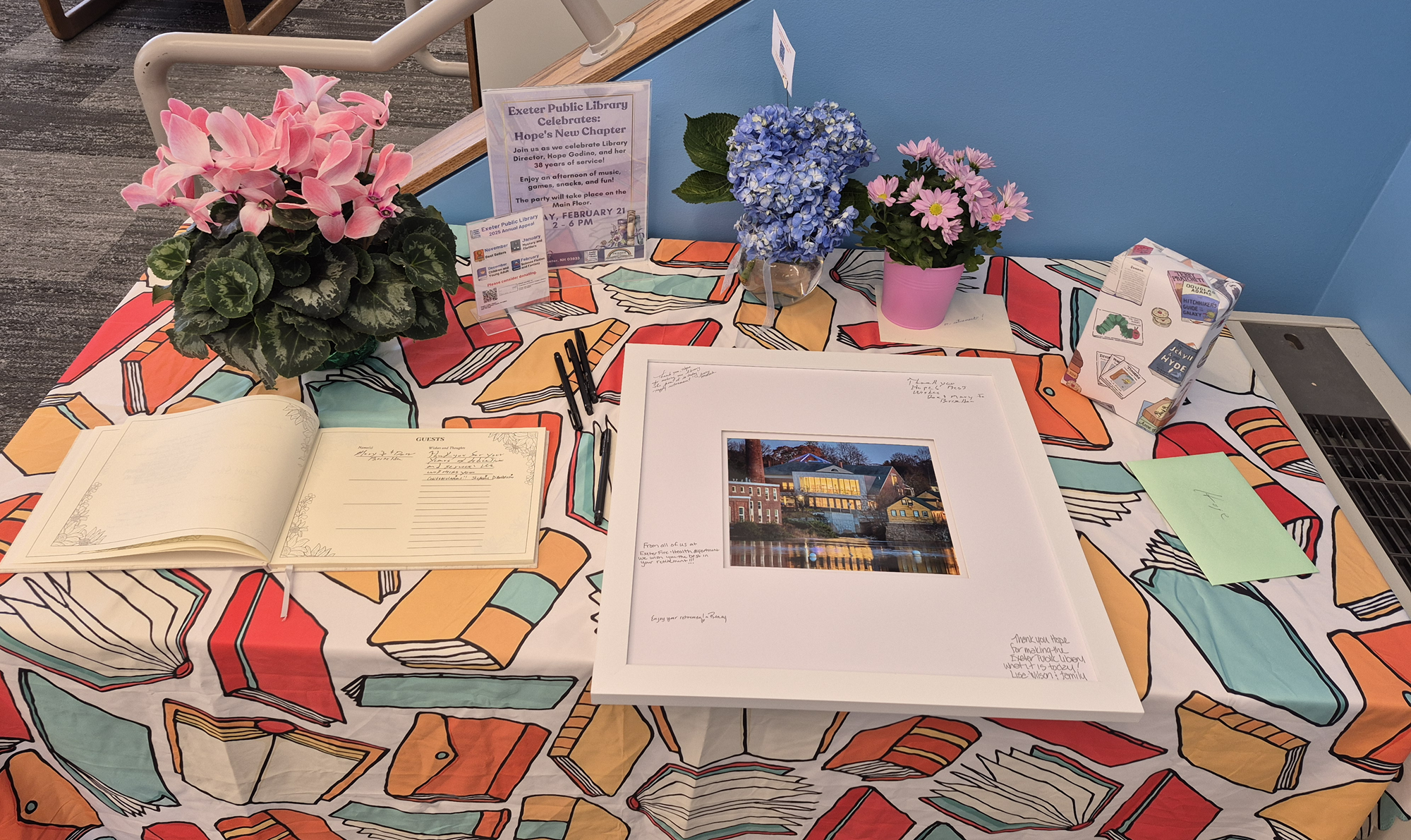 Flowers, a guest book, cards, greeting cards, presents, and a photo of the library with signatures and well wishes at Director Hope Godino's Retirement Party Flowers, a guest book, cards, greeting cards, presents, and a photo of the library with signatures and well wishes at Director Hope Godino's Retirement Party