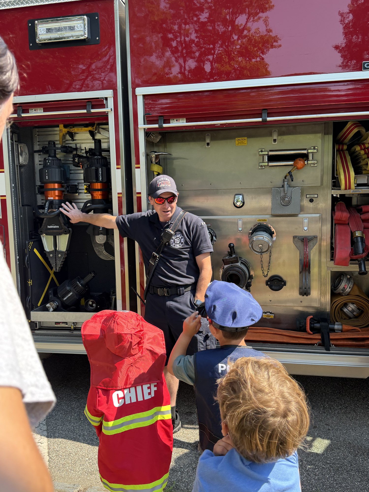 Patrons learning the different parts of a fire truck with a firefighter during Touch-a-Truck.
