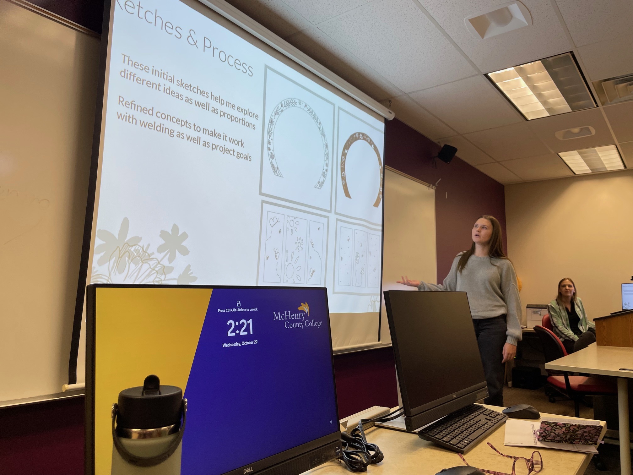 Student standing in a front of a screen showing drawings of her design.