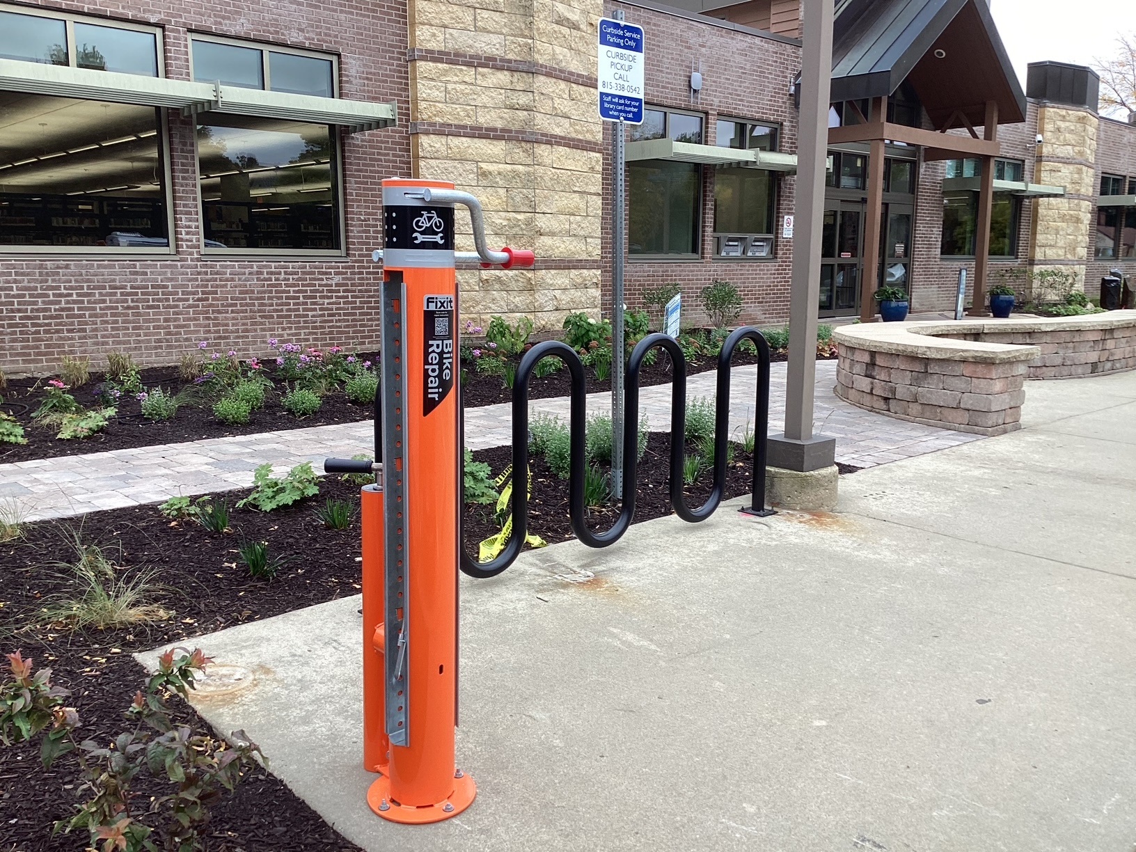 An orange metal pillar with bike repair tools next to a bike rack by the library entrance.