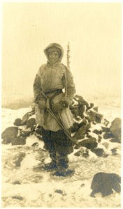 sepia photo of a woman in standing in the snow in snowshoes and a fawn skin coat