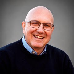 smiling bald white man in glasses and a dark sweater 