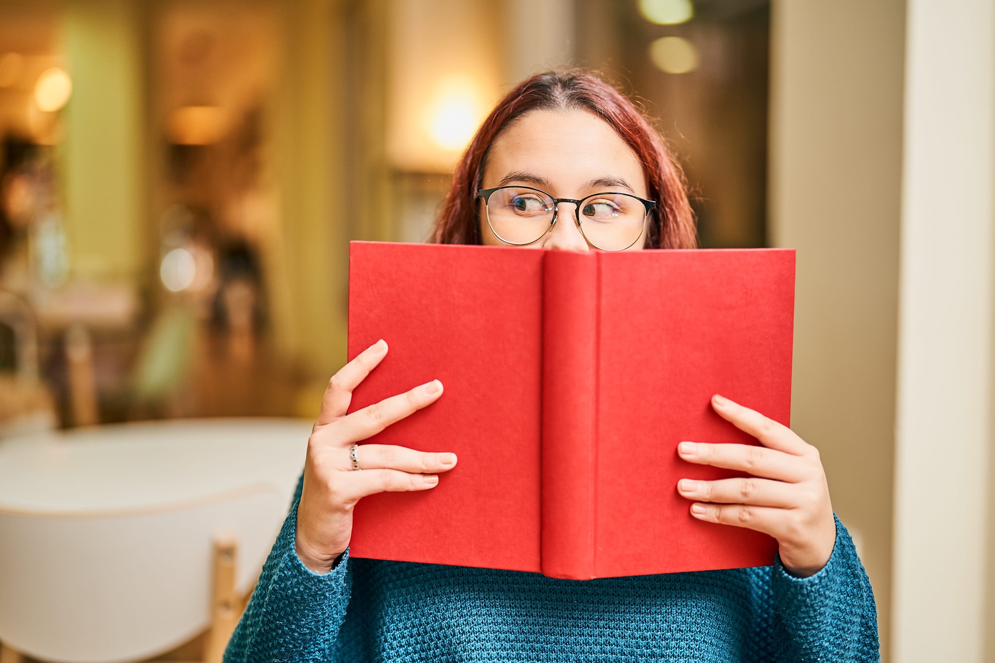 Young Woman Hiding Her Face Behind A Red Book And Looking Sideways
