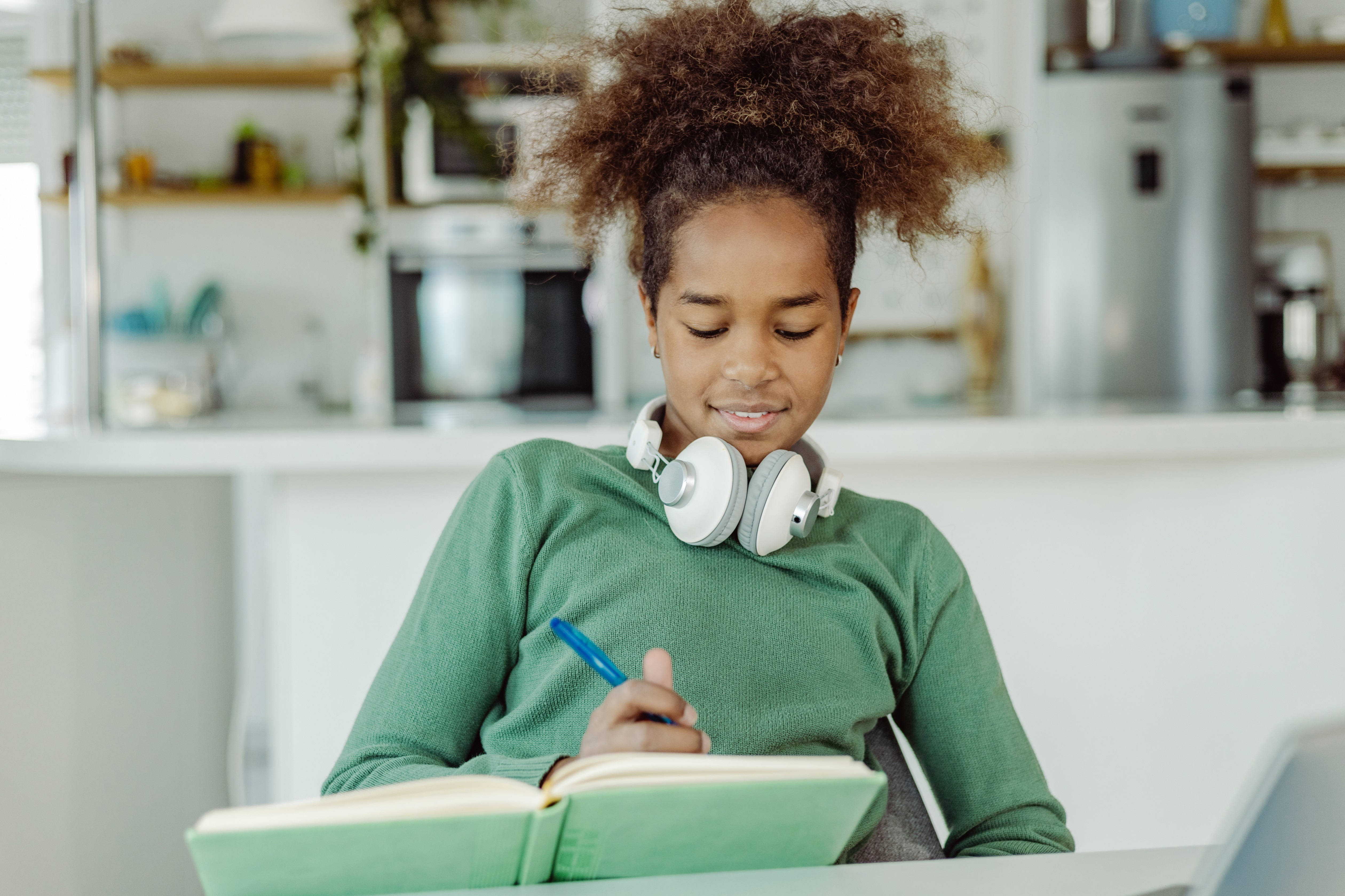Teenage girl wearing headphones around her neck writing in a journal. 