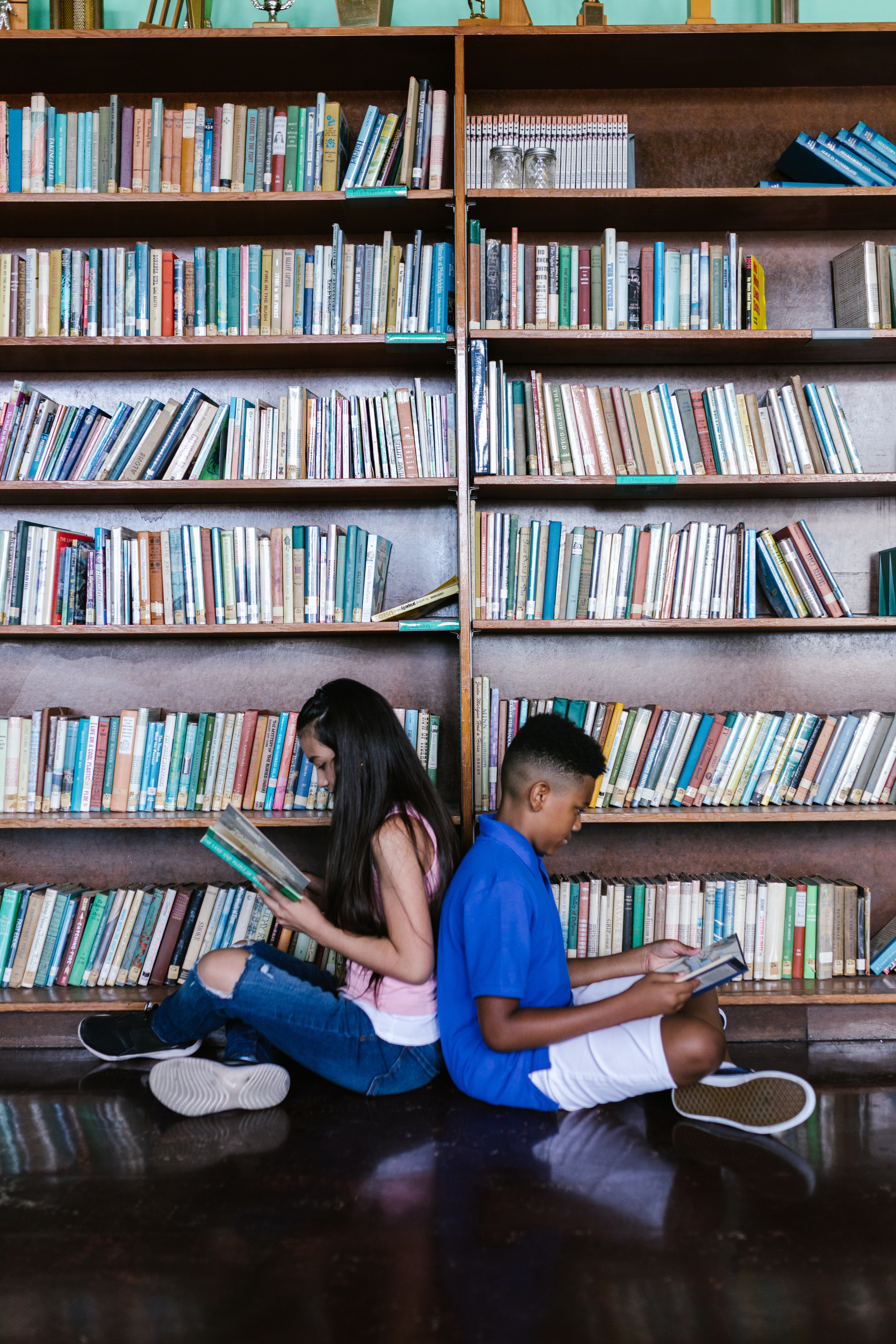 Teen and child sitting back to back reading a book. 