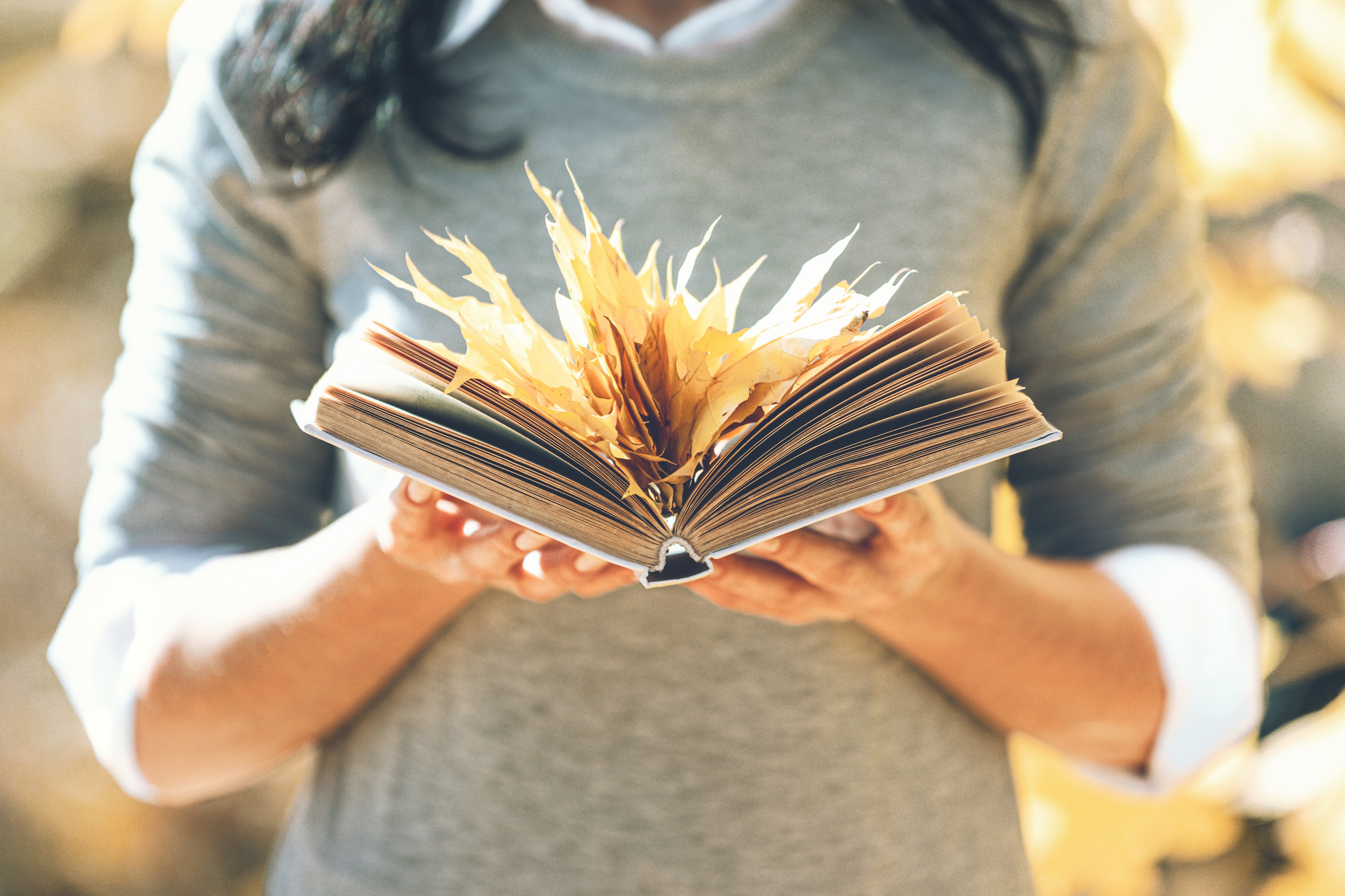 Woman holding an open book with fall leaves in the centre. 