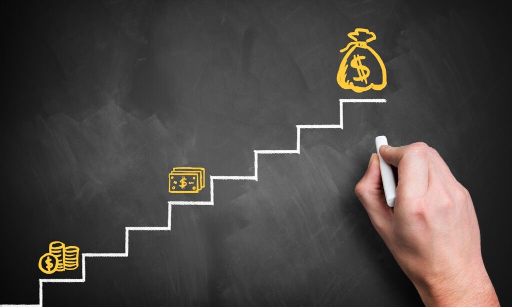 A chalkboard drawing of steps with a bag of money at the top