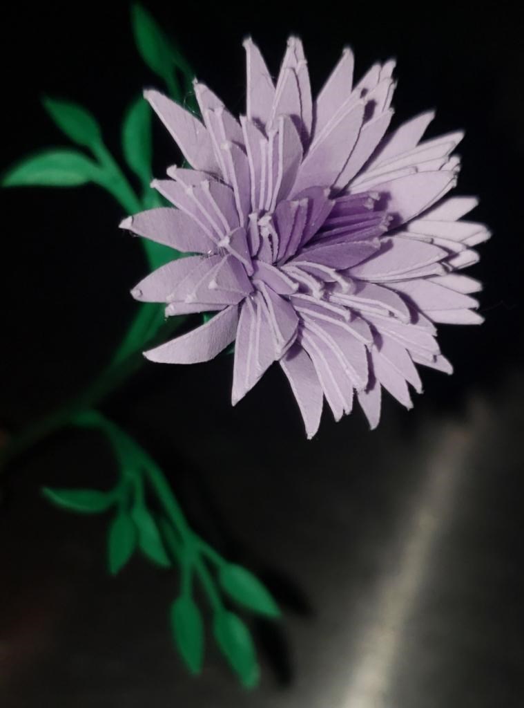 A lavender colored paper flower with a green stem