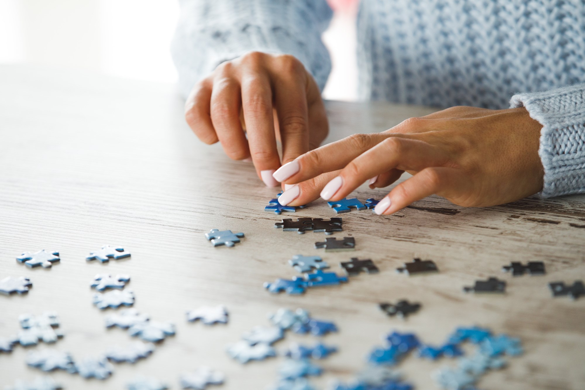 Close up of Female Hands Playing with Puzzle Pieces on Wooden Table