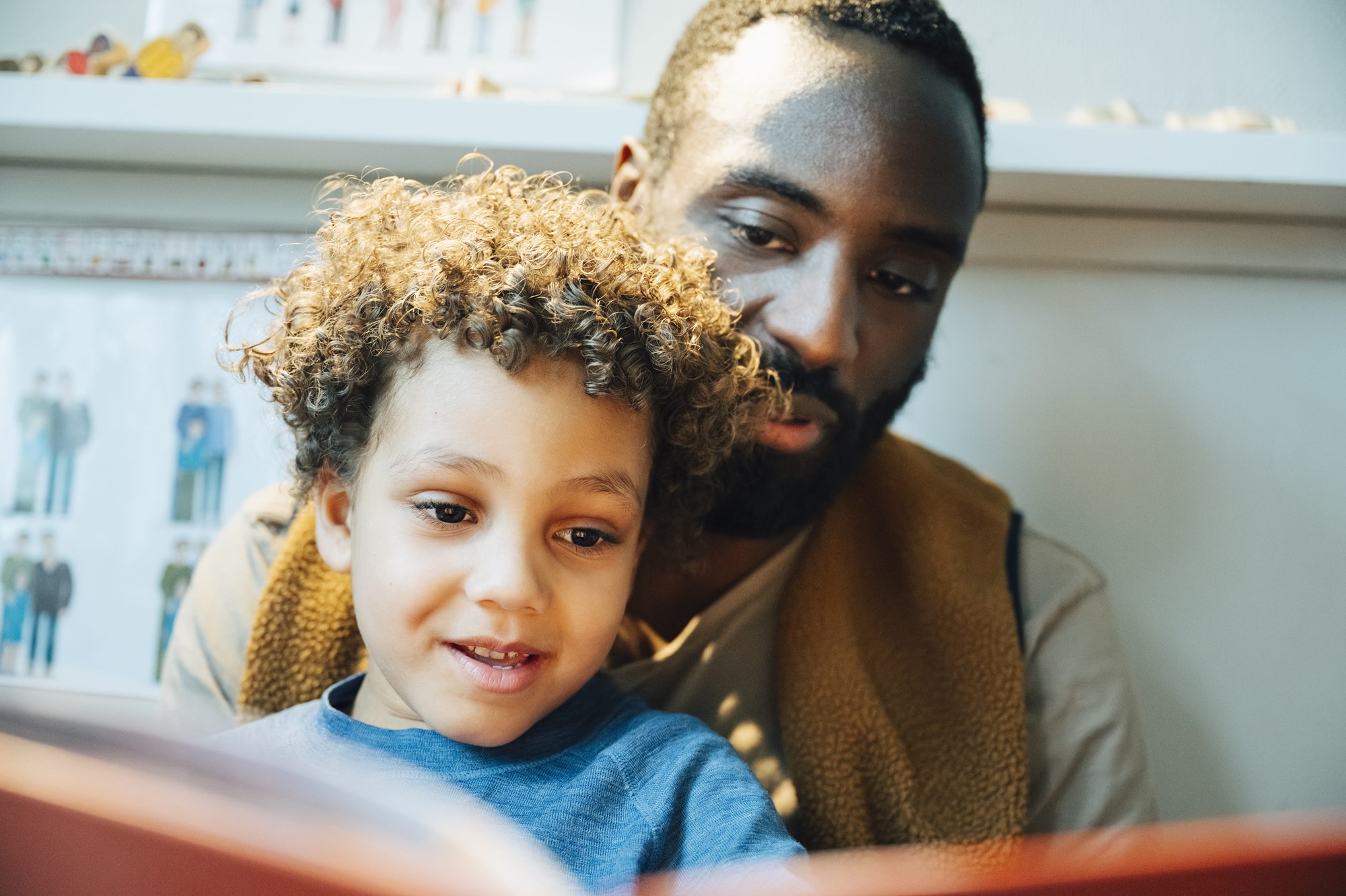 Male Teacher and Boy Reading Book While Sitting in Kindergarten Classroom