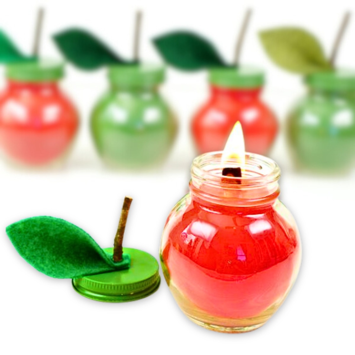 Picture shows a small red candle in a jar with a green lid sitting to the side. The green lid has a stem and leaf mimicing an apple.