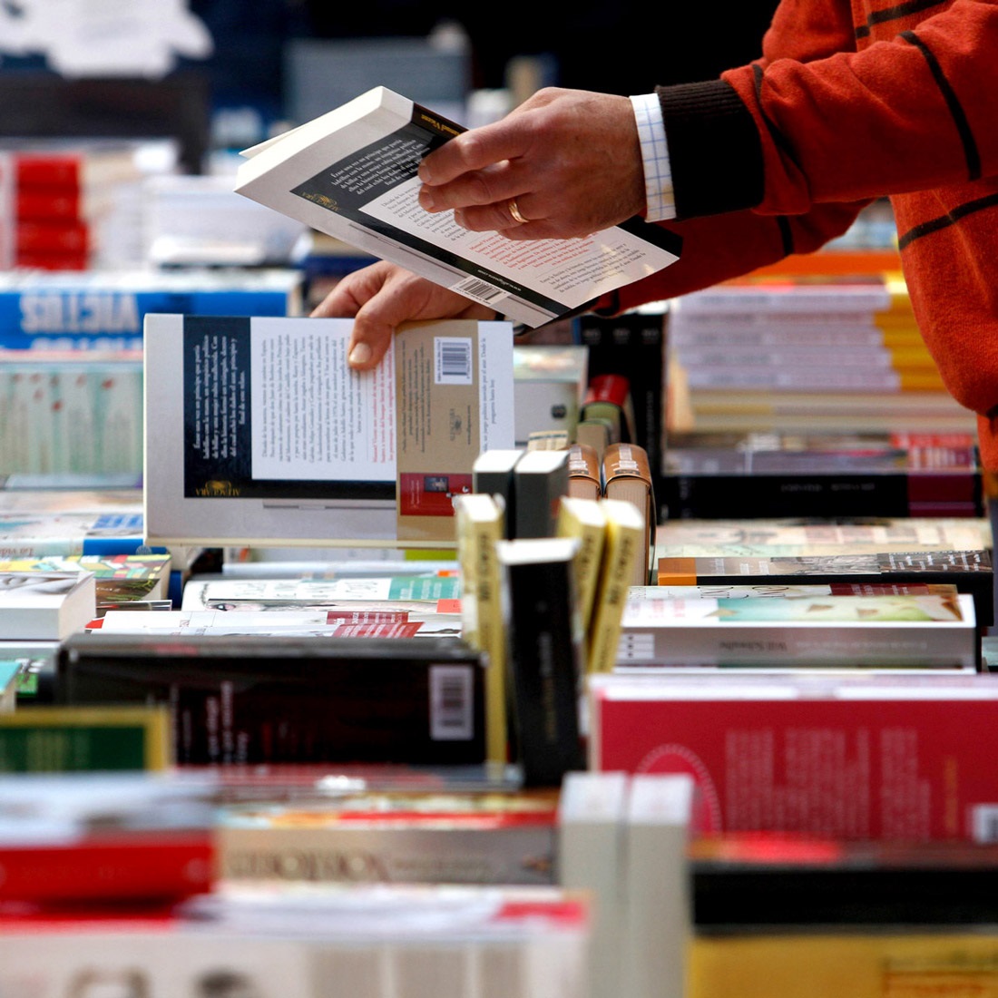 Person browsing books in a table. Link opens in new tab or window.
