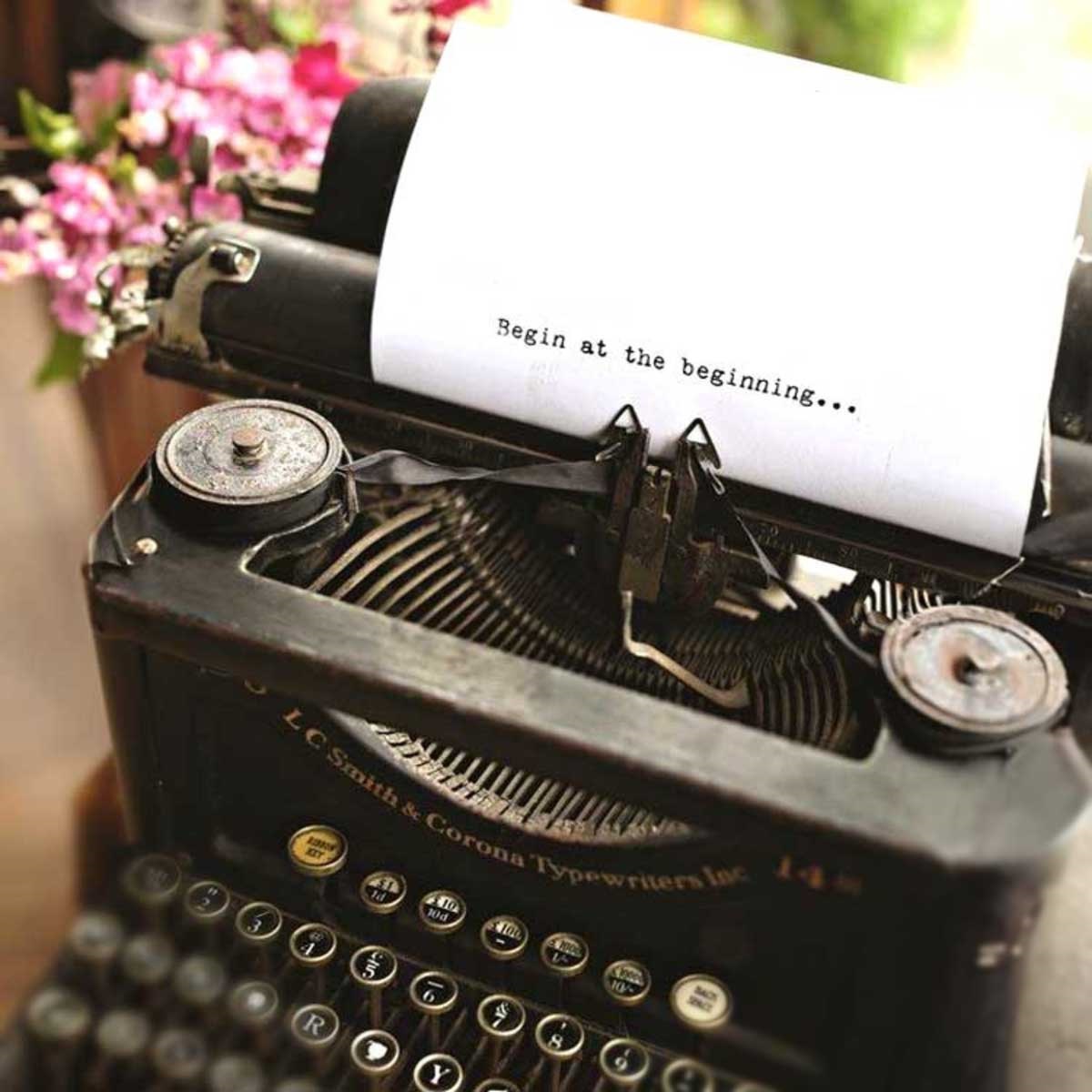 A vintage Corona typewriter, a paper in it with the words typed: Begin at the beginning...