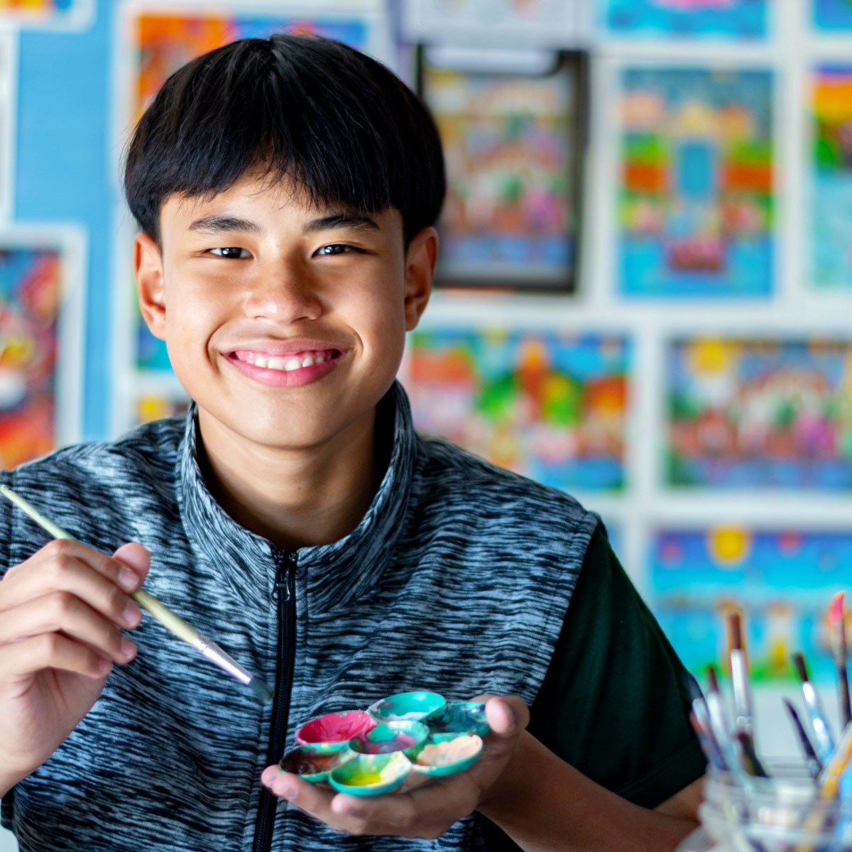 Asian teen smiling with a paintbrush in his hand