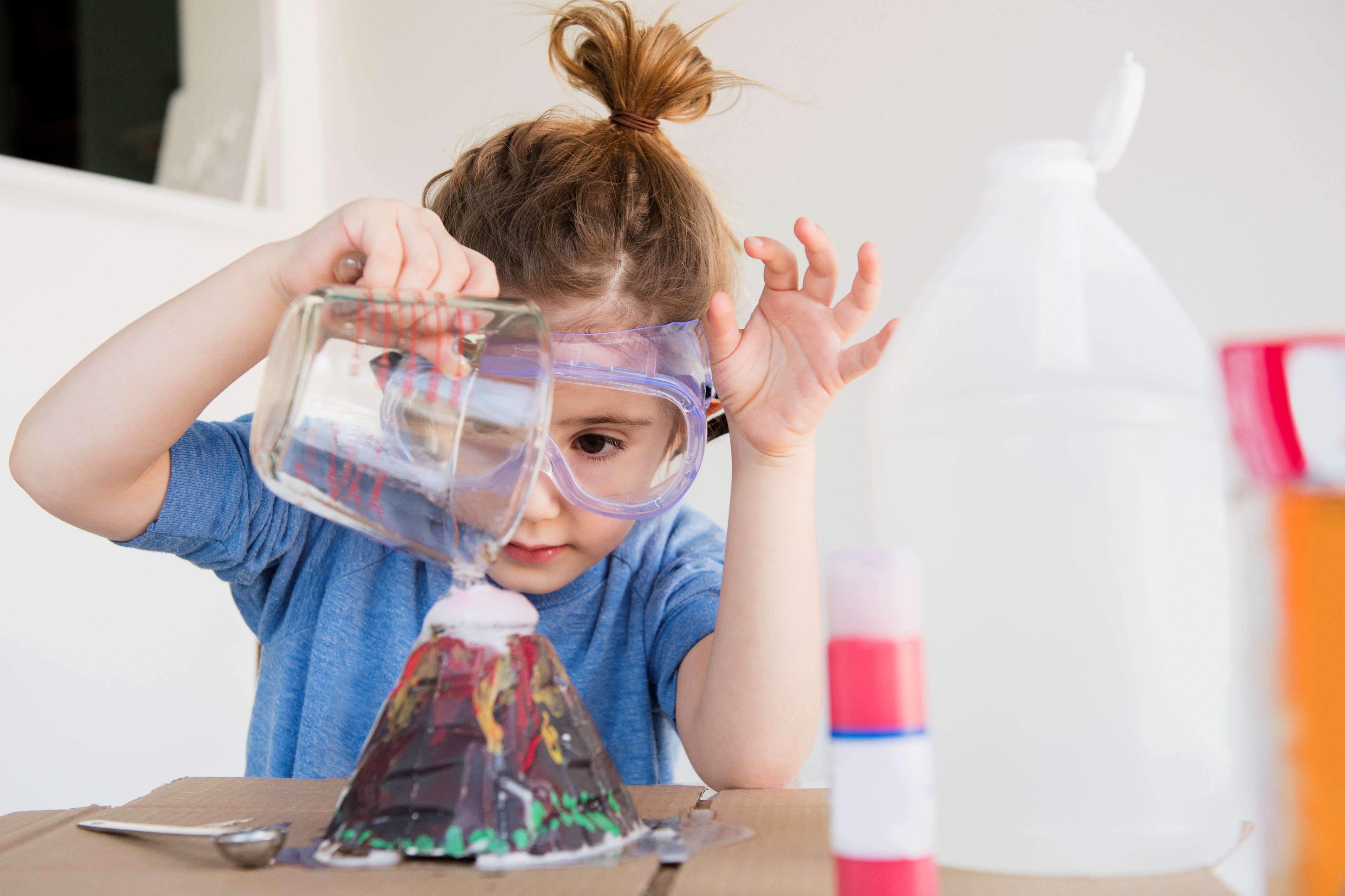 young girl wearing safety goggles pouring liquid into a model volcano
