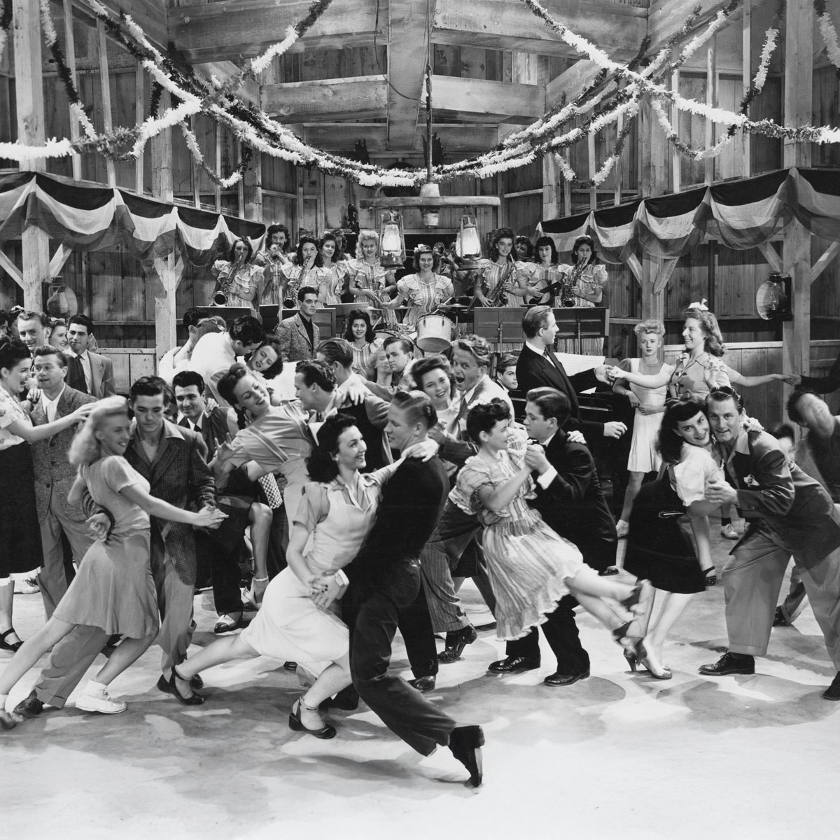 image is a black and white photograph of many couples dancing in a dance hall.