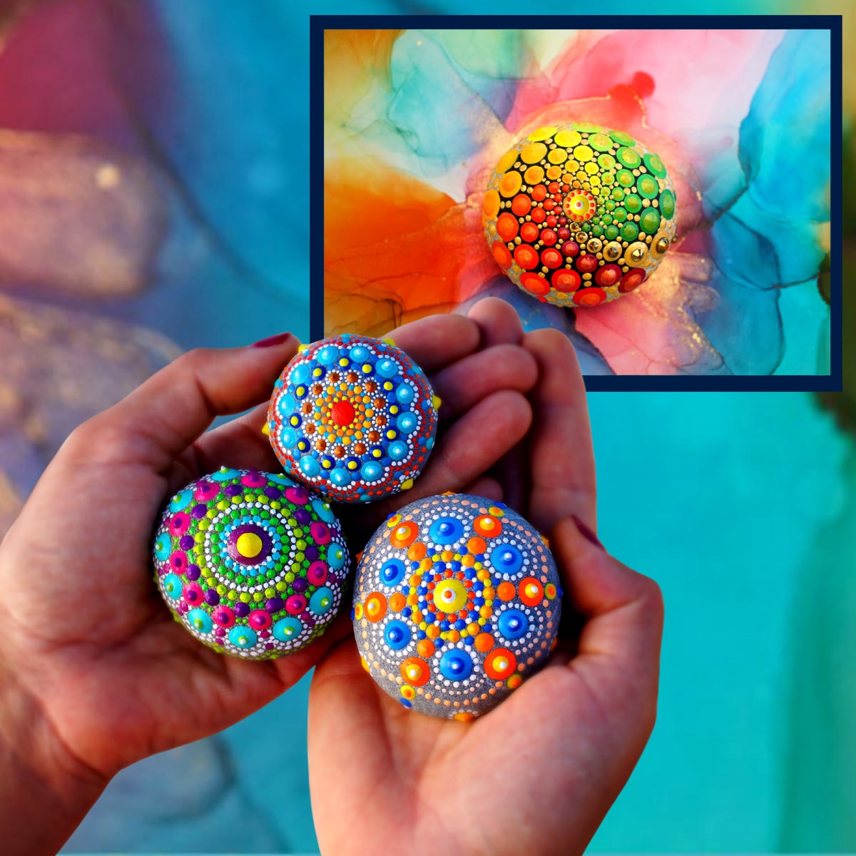 On a tie-dye bakcground two hands hold three rocks painted with colorful mandalas.