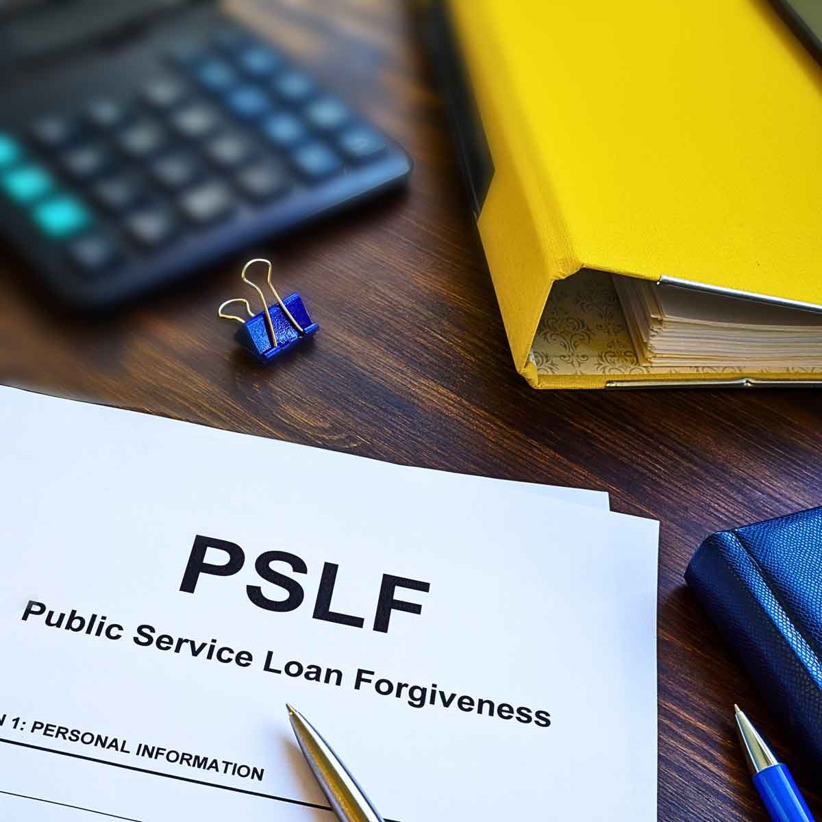 Image depicts a paper titled PSLF on a desk.  There is also a calculator in the top left corner, and part of a yellow binder on the top right corner.
