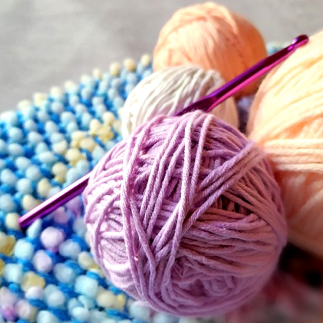 There are three balls of yarn with a crochet needle through the front most ball.
