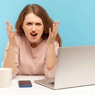 Image depicts a woman frustrated with her laptop and/or phone.