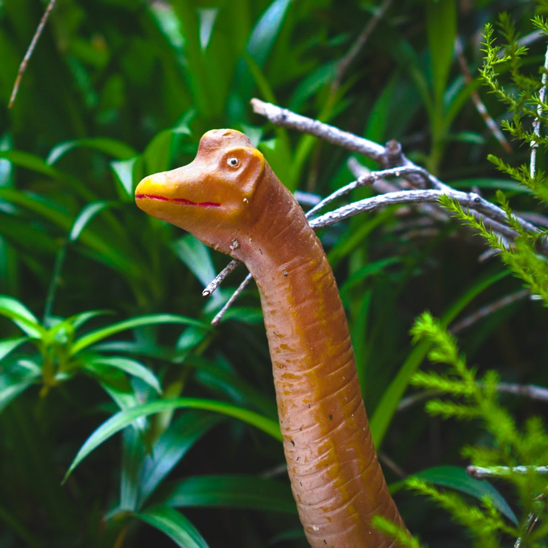A cute dinosaur toy in tall grass.