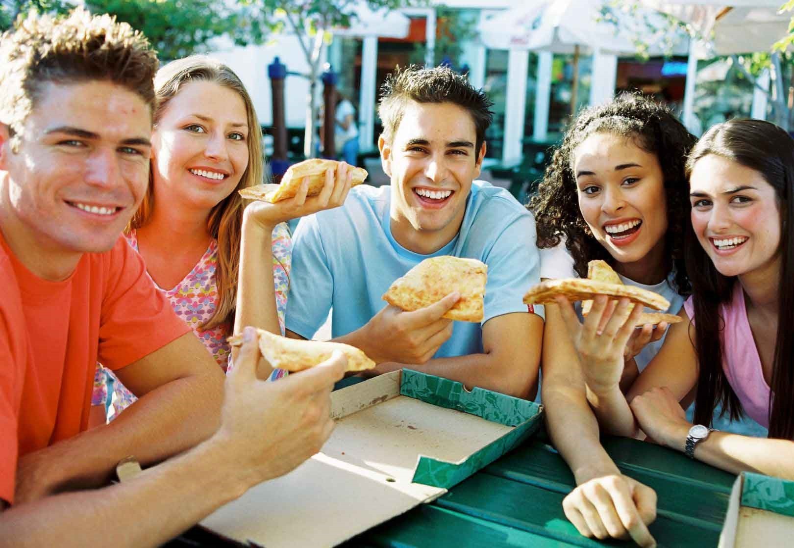five teens smiling and eating pizza