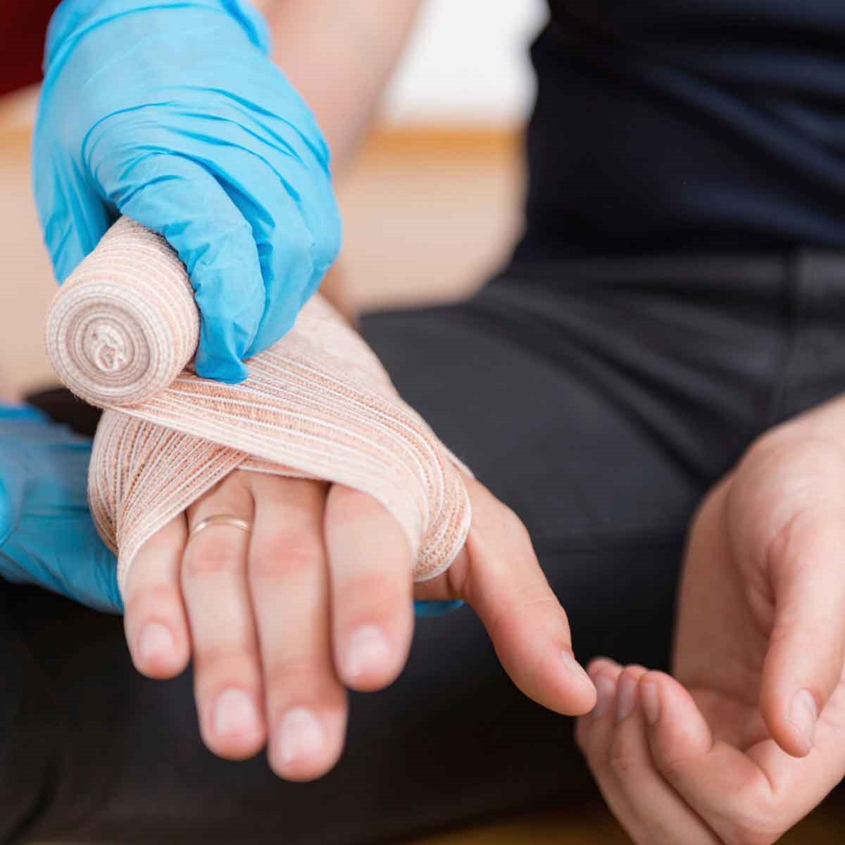 Image is of a man's hand being wrapped by a hand in blue gloves.