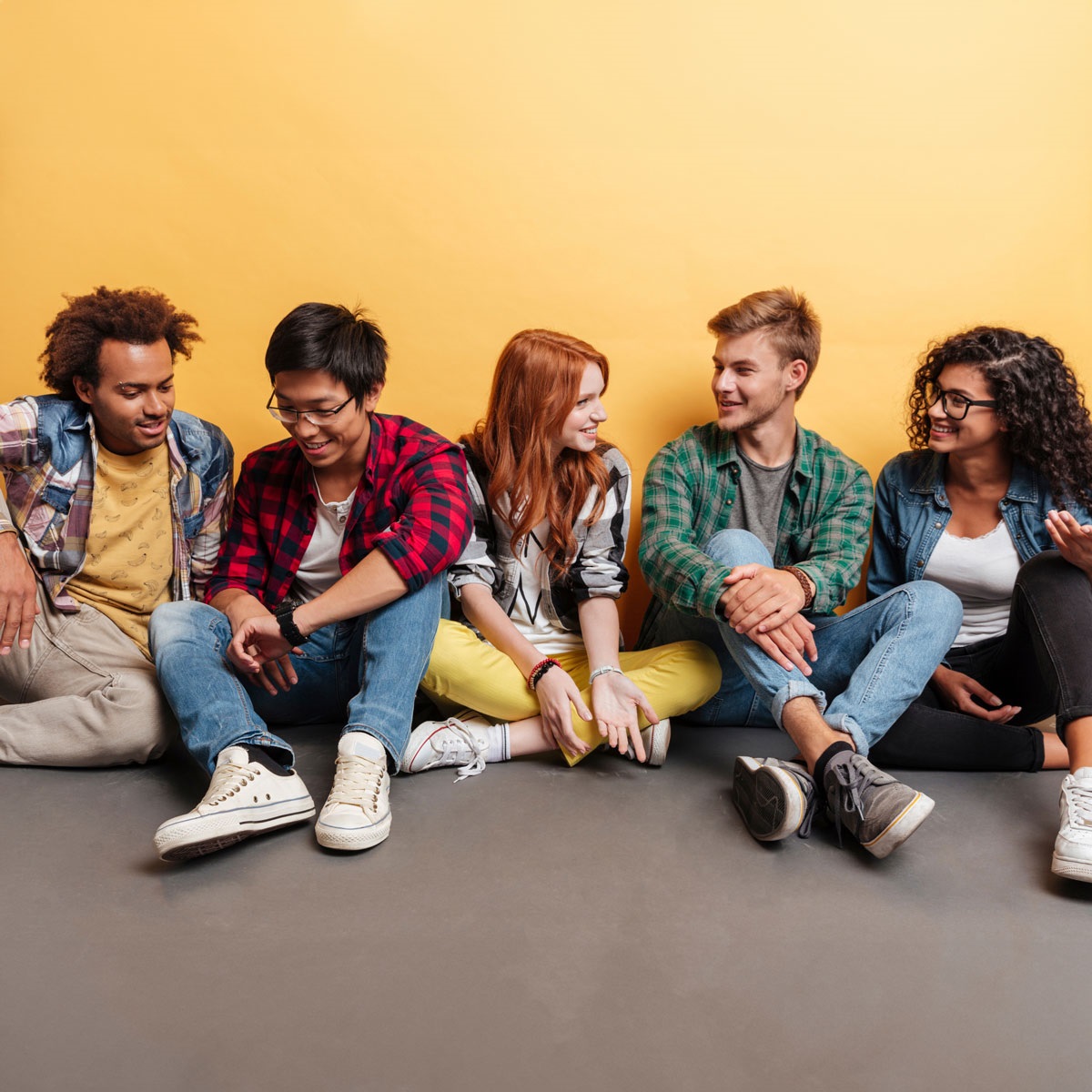 group of 5 young adults sitting on the floor talking