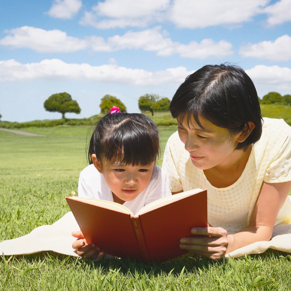 A mom reading with her daughter at the park on a beautiful summer sunny day for Bilingual Storytime. 