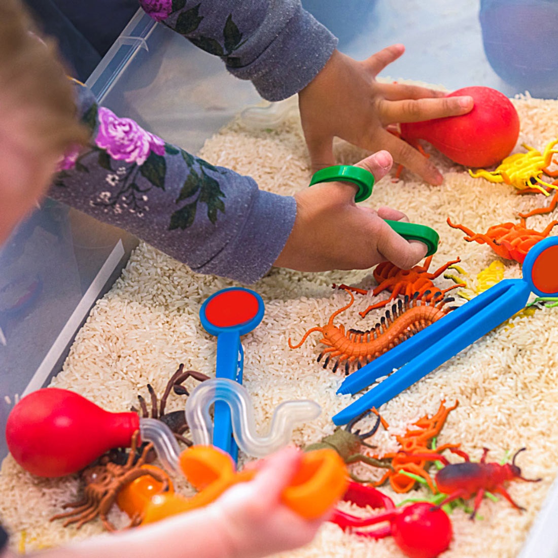 Children playing with toys in a container filled with rice for our Sensory Play event.