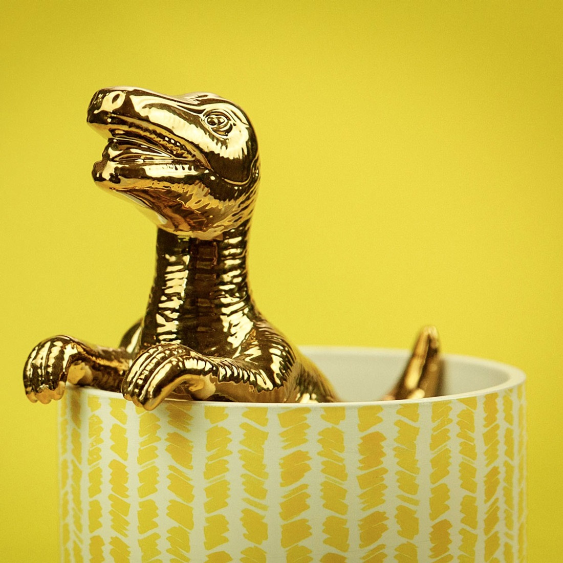 A shiny gold T-Rex toy in a tea cup.