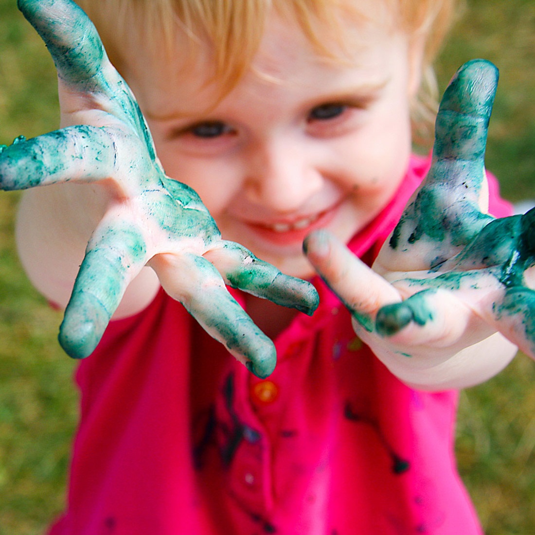 Cute smiling, little girl, showing the paint she has all over her hands and fingers for a fun Totally Untidy Tots event!