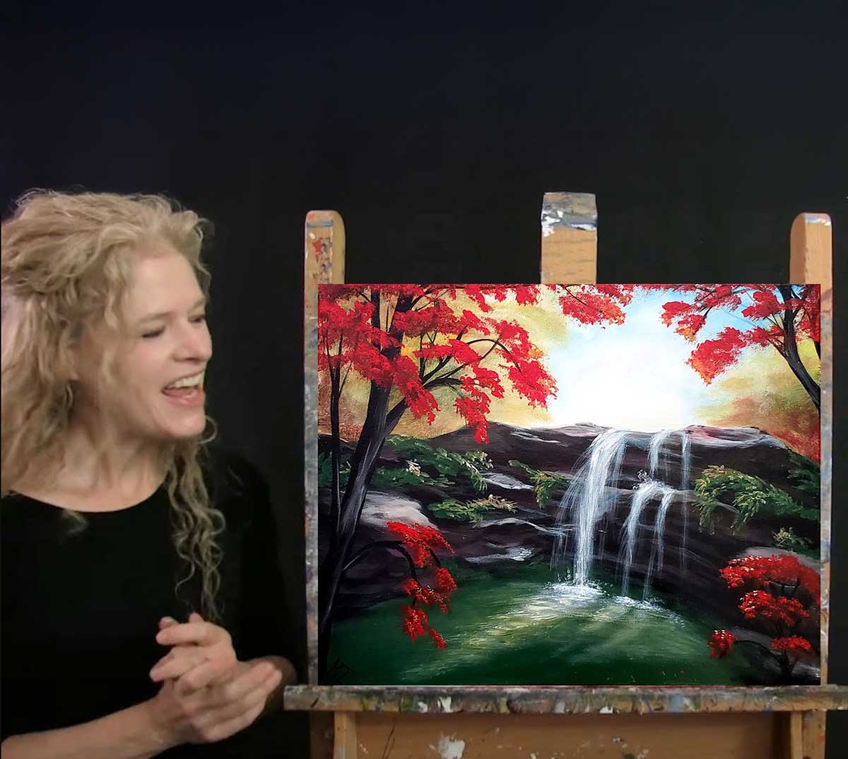 Image shows Michelle the painter standing next to her painting, "waterfall in fall."