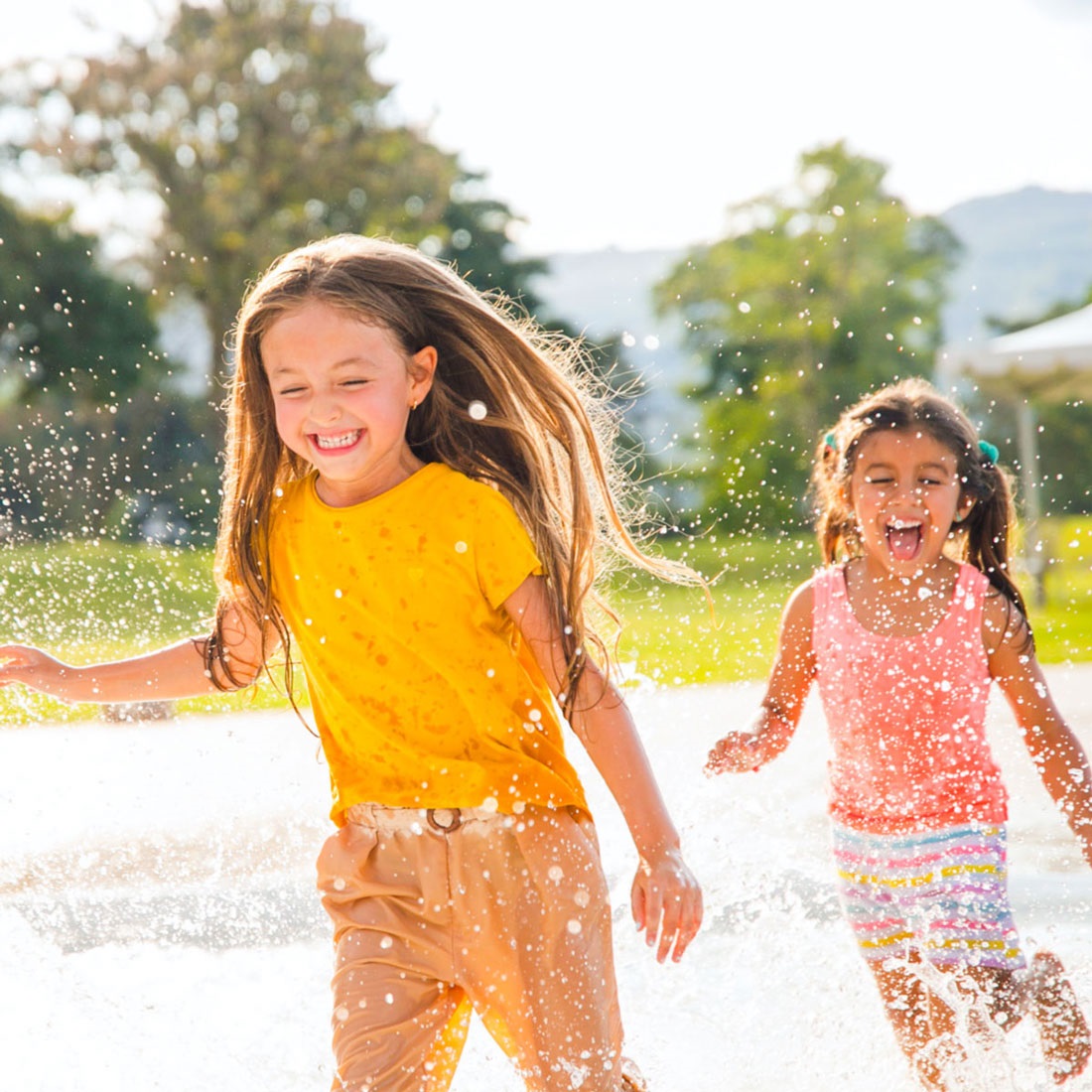Two girls laughing and running at our Splashpad STEAM event.