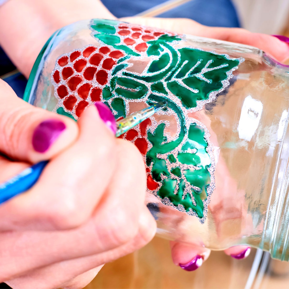 A woman painting a jar to look like it has a stained glass design.