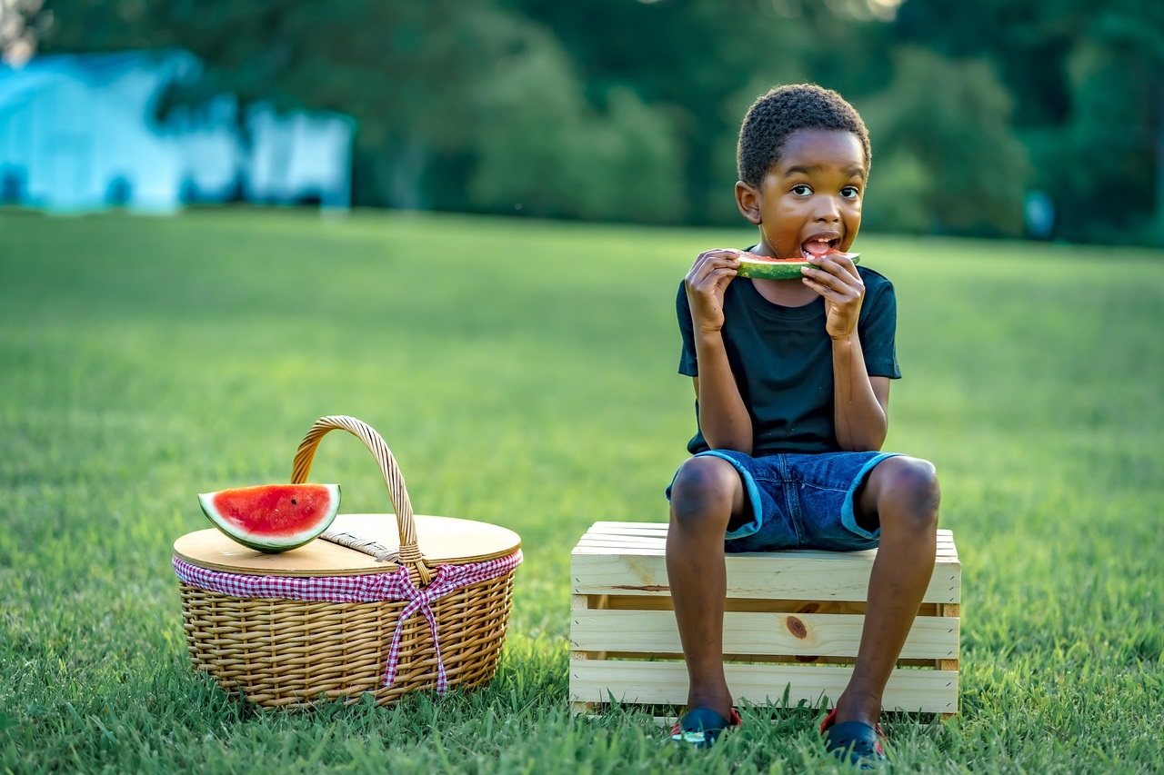 African American boy sitting on a crate eating watermelon