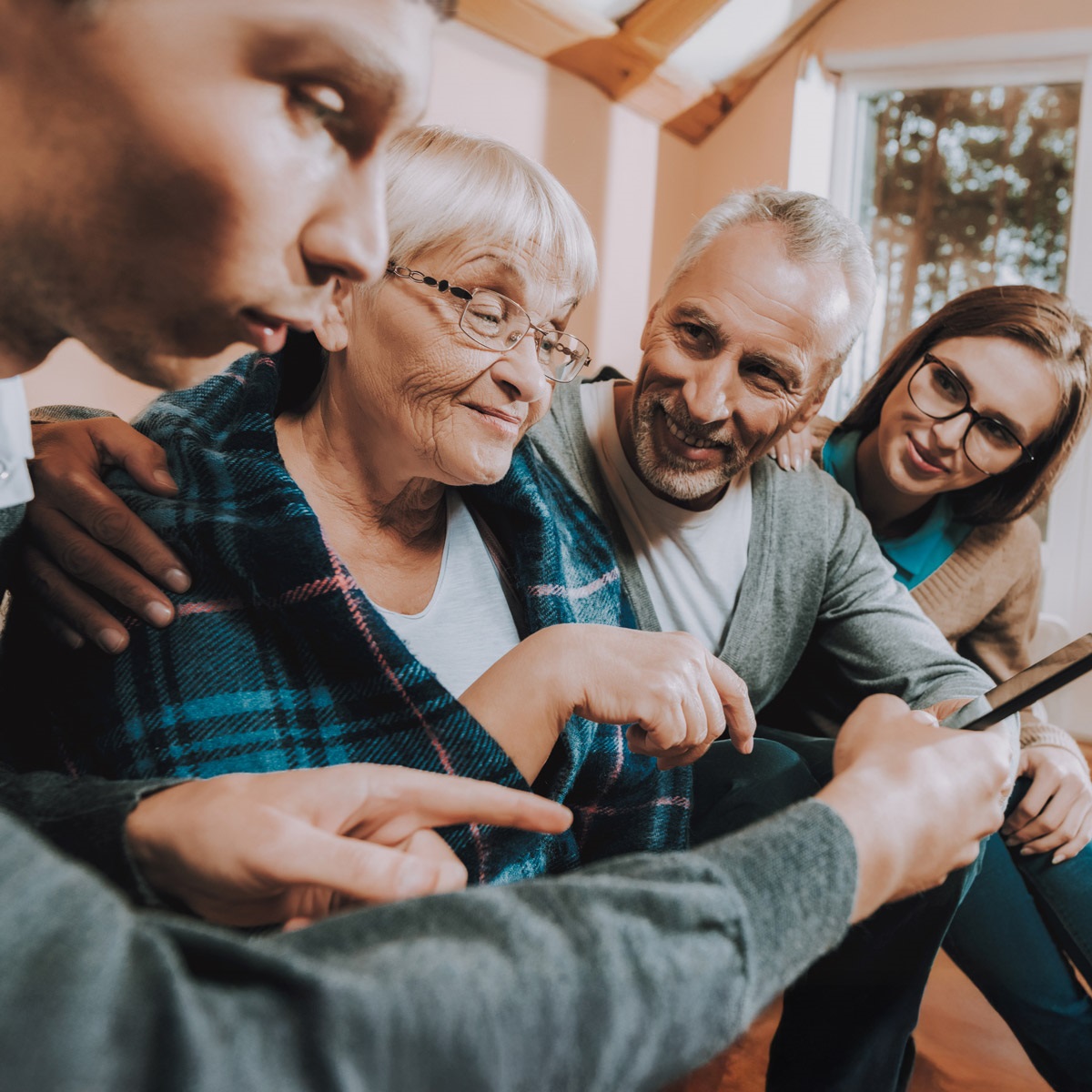 Image depicts a pair of older folks and 2 younger people all looking at a phone.
