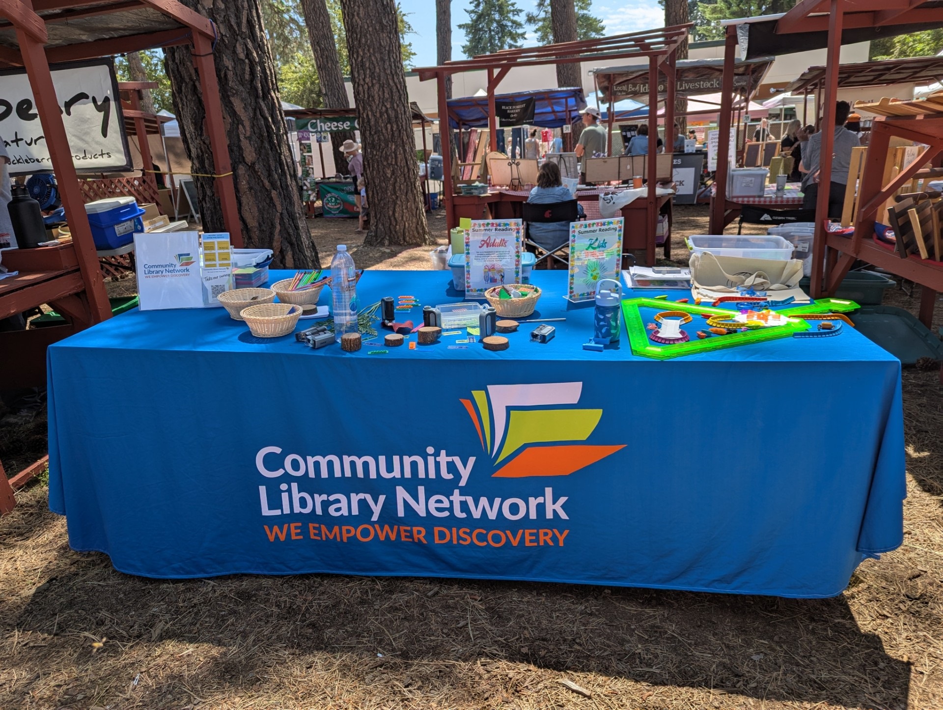 CLN table at a farmers market--CLN bright blue table cloth and several items cover the table.