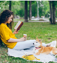 Images of a woman in a park reading. She is on a blanket, leaning up against a tree.  Next to her is her medium-sized dog.