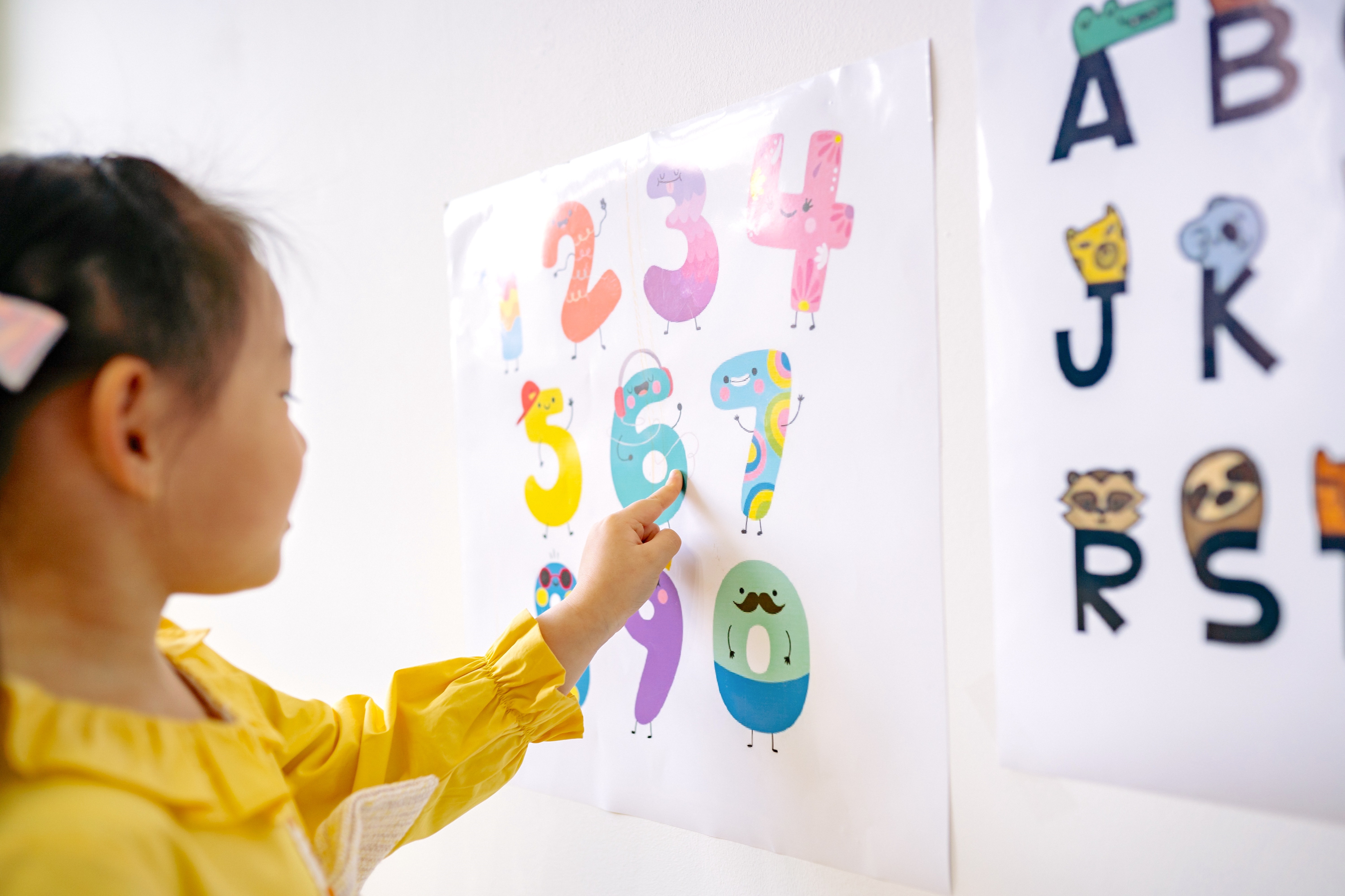 Image of a young girl in a yellow dress tracing numbers on a wall.