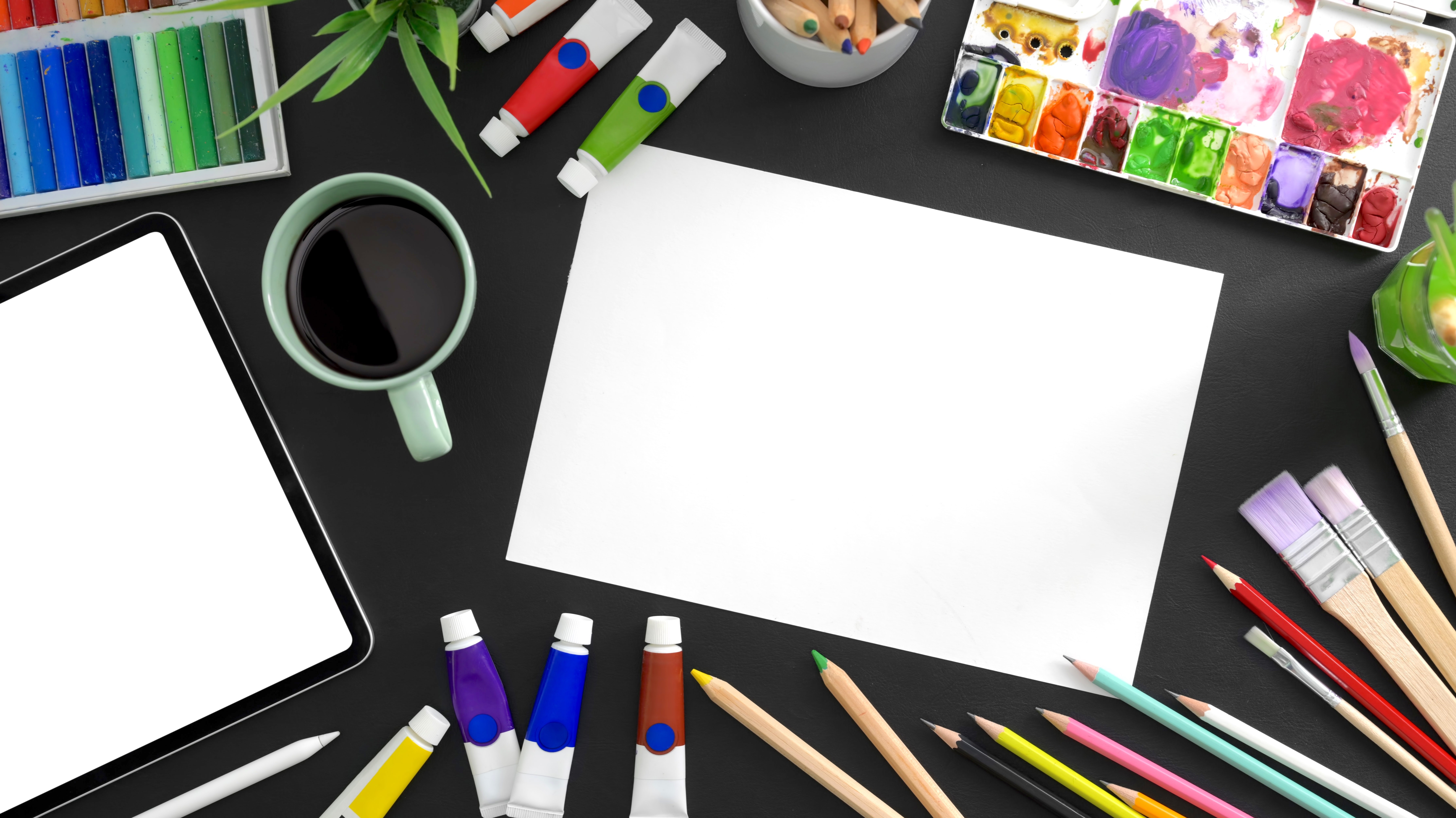 assorted art supplies around a blank piece of white paper