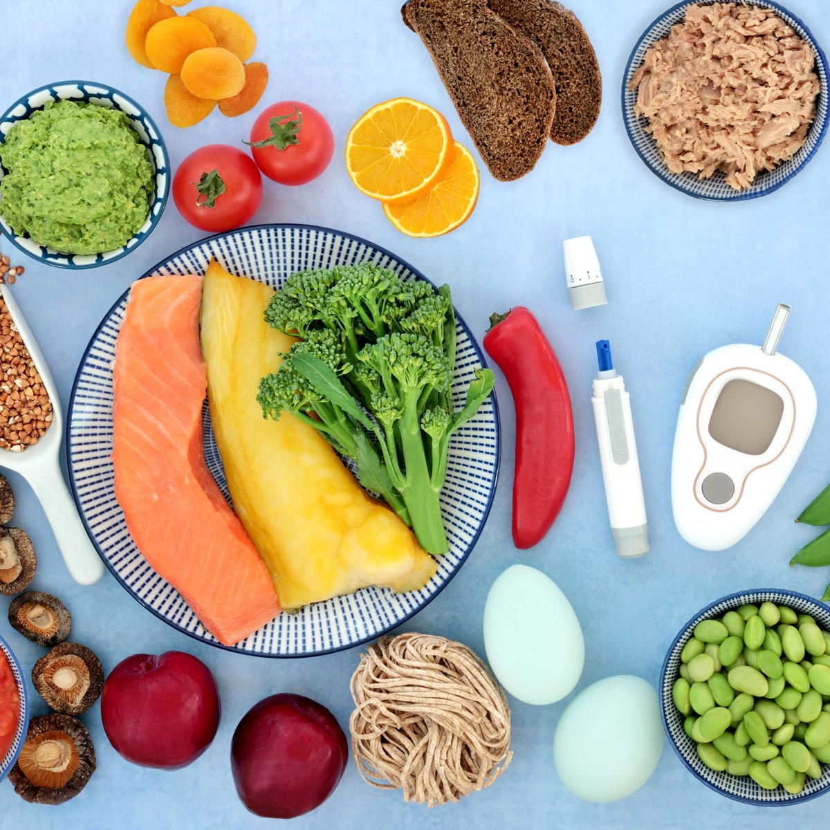 On a blue background there is a variety of healthy foods.  On the right side among the food is also a blood sugar monitor.
