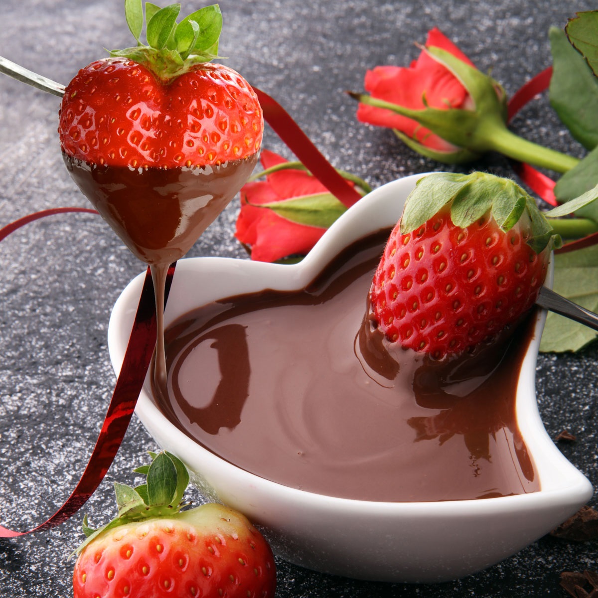 Heart shaped bowl filled with chocolate and strawberries being dipped in.
